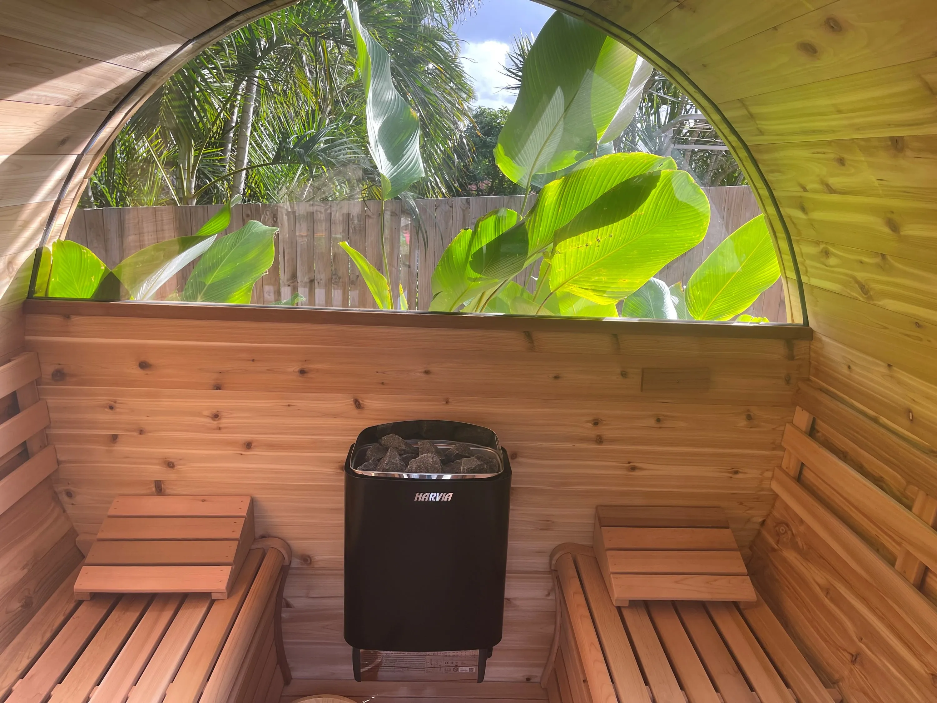 Inside the barrel sauna, a heater between benches under a half-moon garden window