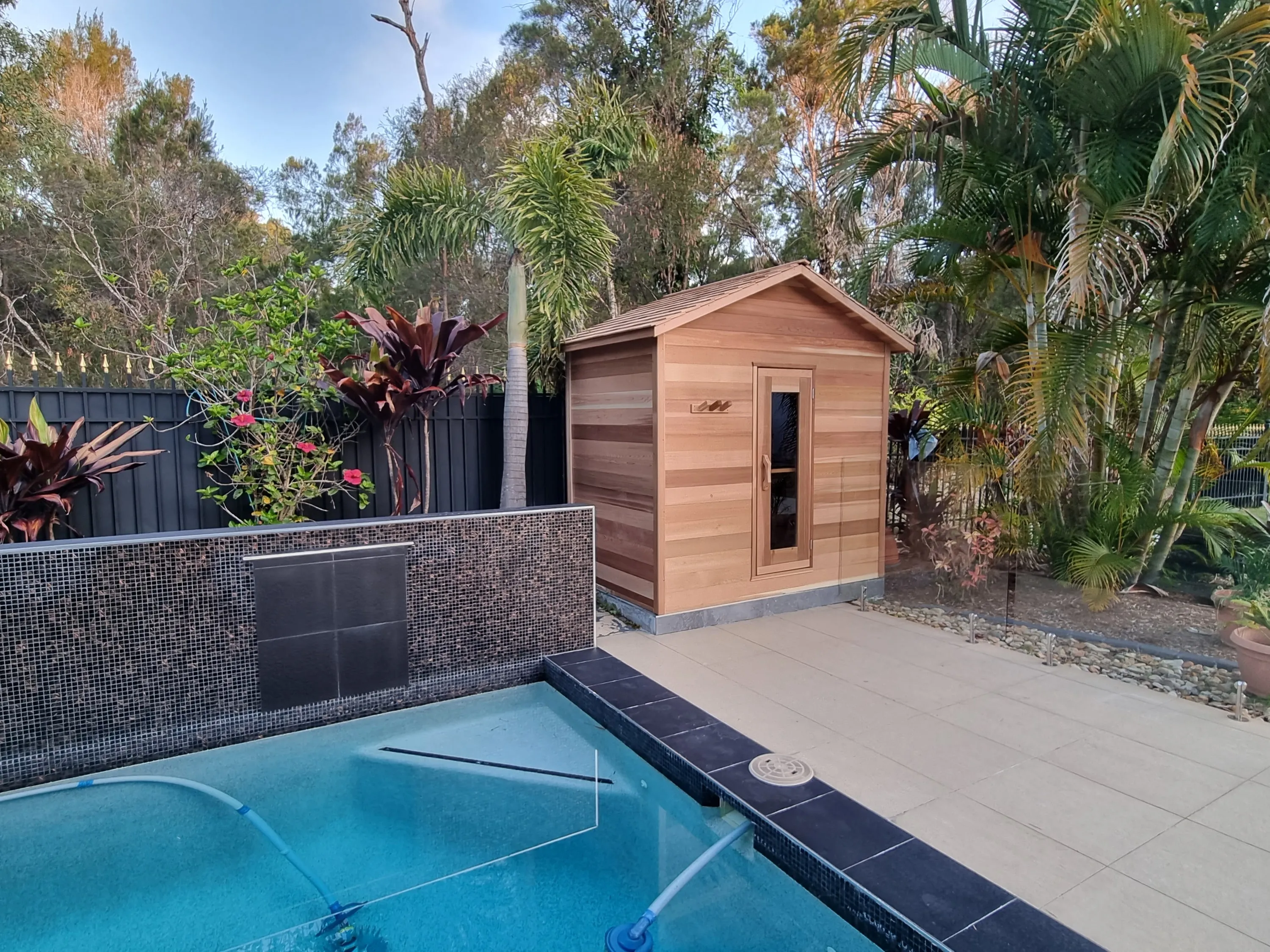 Timber cabin sauna beyond the pool and stone wall