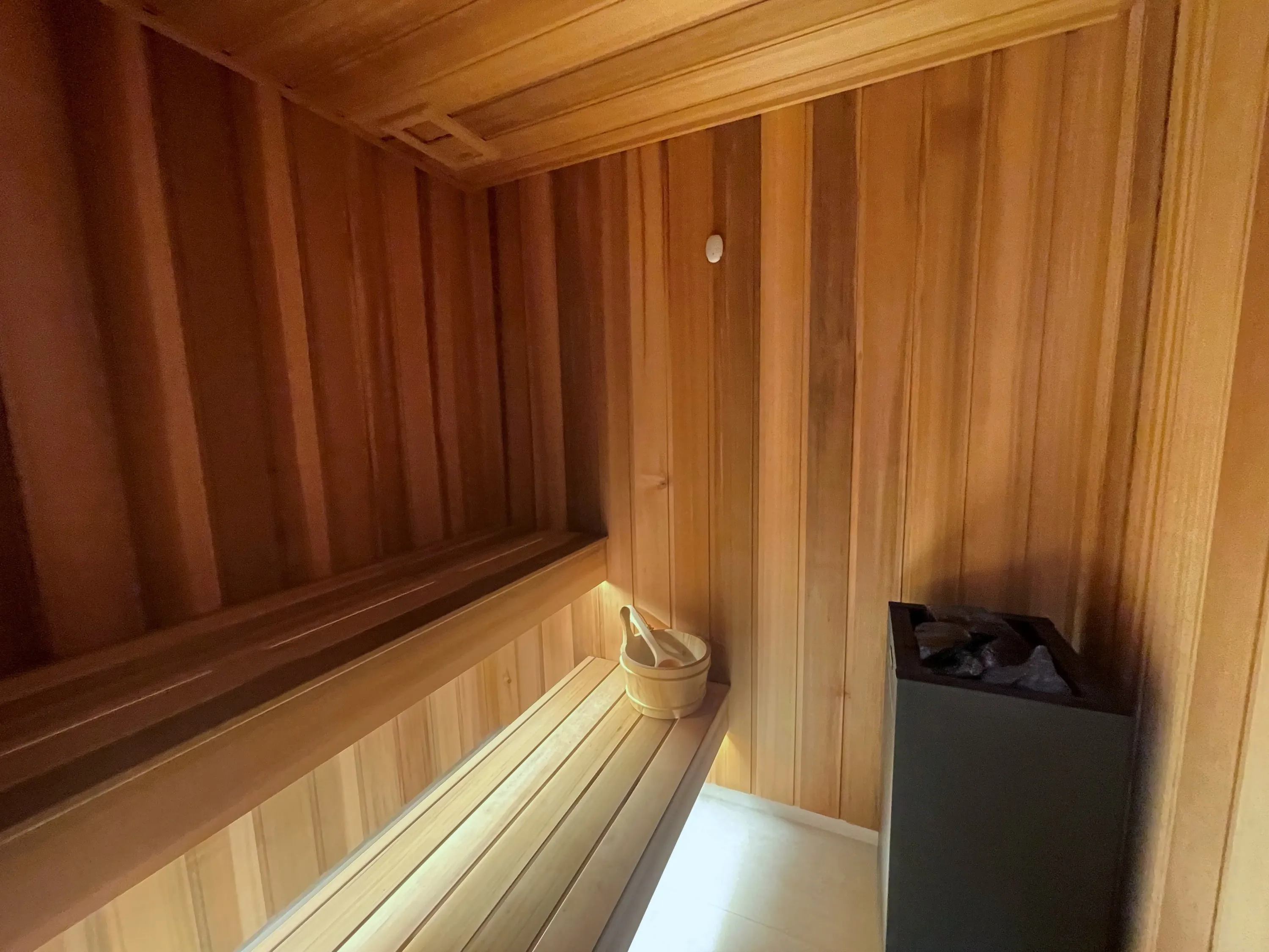 Timber sauna with lit benches and a floor-standing heater filled with stones