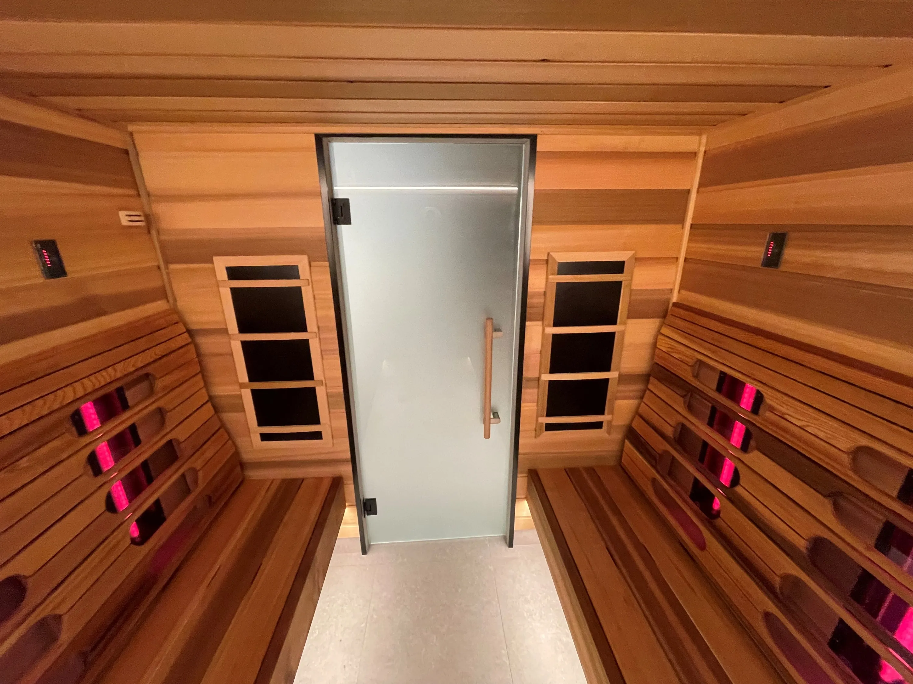 Infrared sauna seen towards a frosted glass door, with emitters glowing behind timber backrests