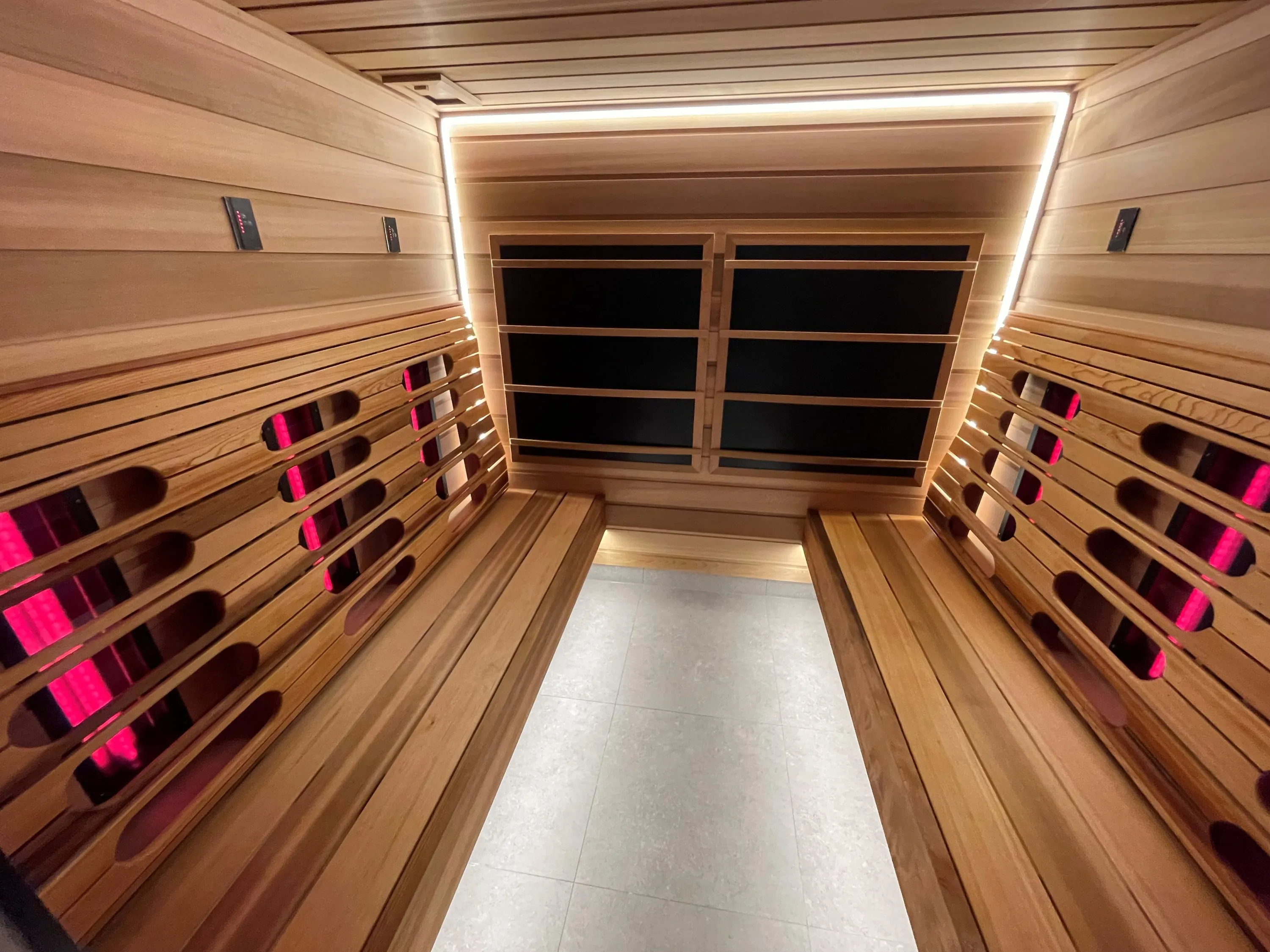 Infrared sauna with slatted timber backrests glowing red and dark panels on the end wall