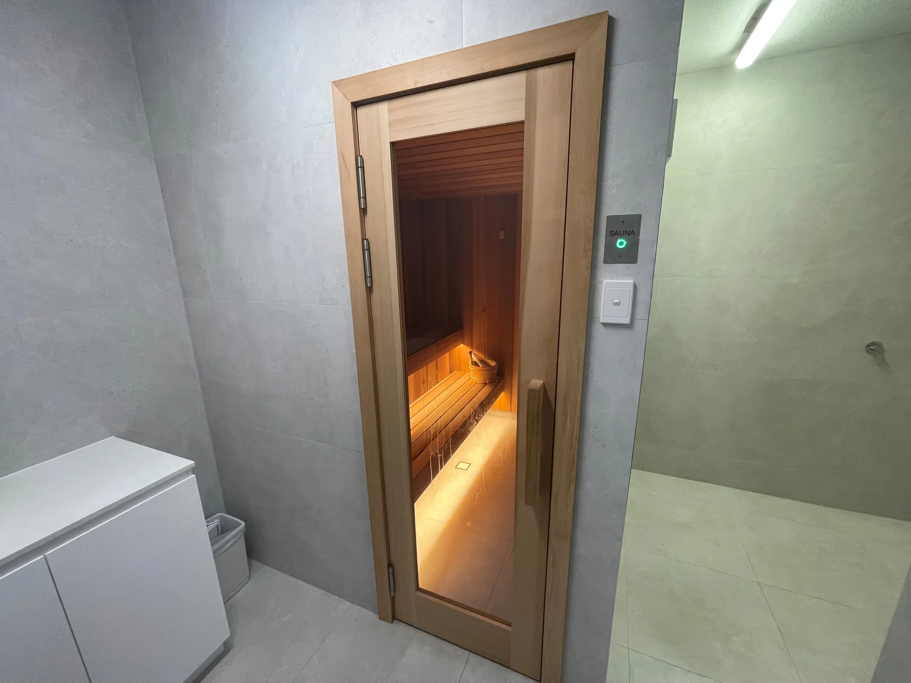 Timber sauna door with a glass panel and a lit SAUNA control plate in a tiled change area