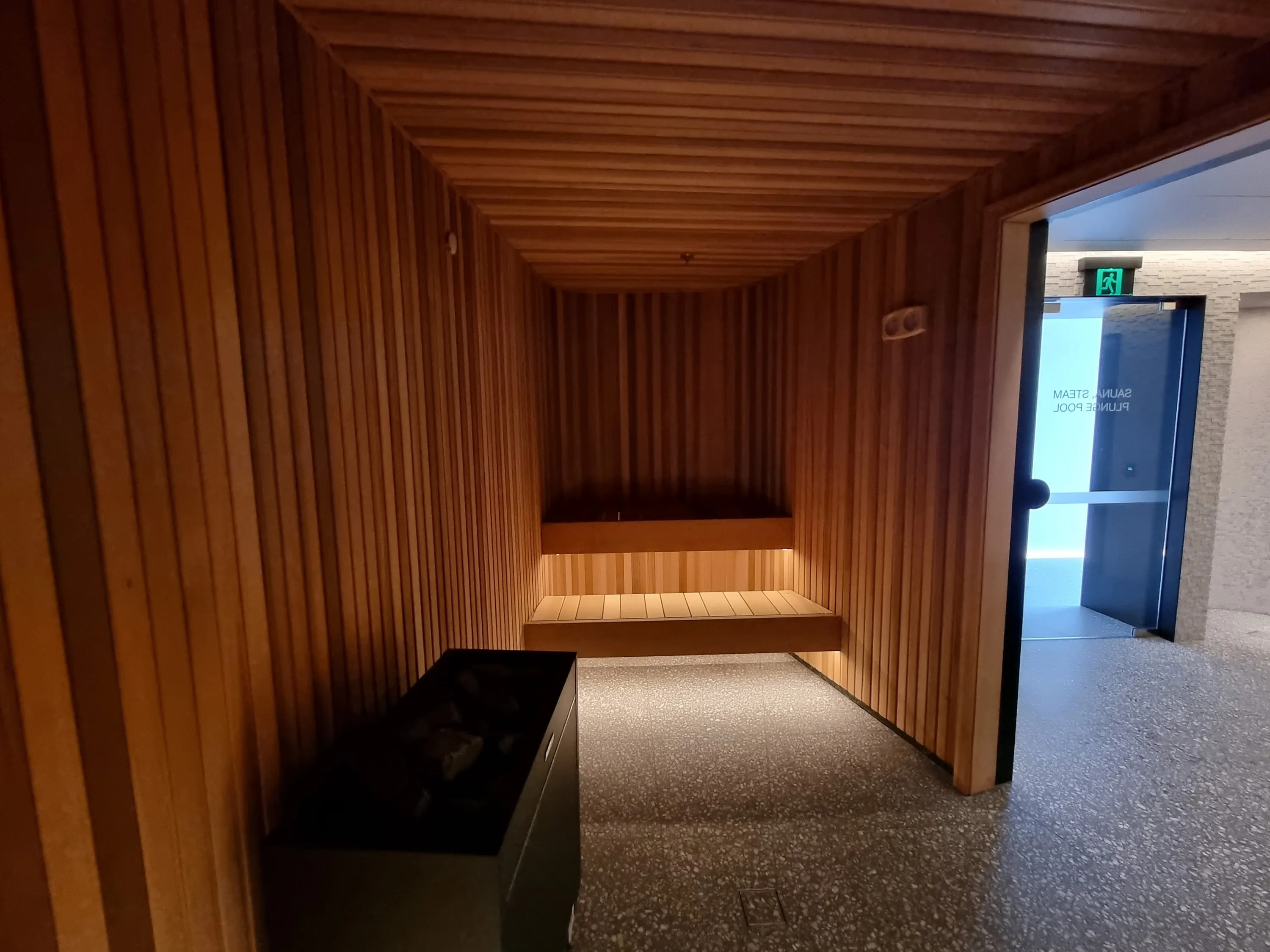 View through the timber sauna towards its open glass door and the corridor