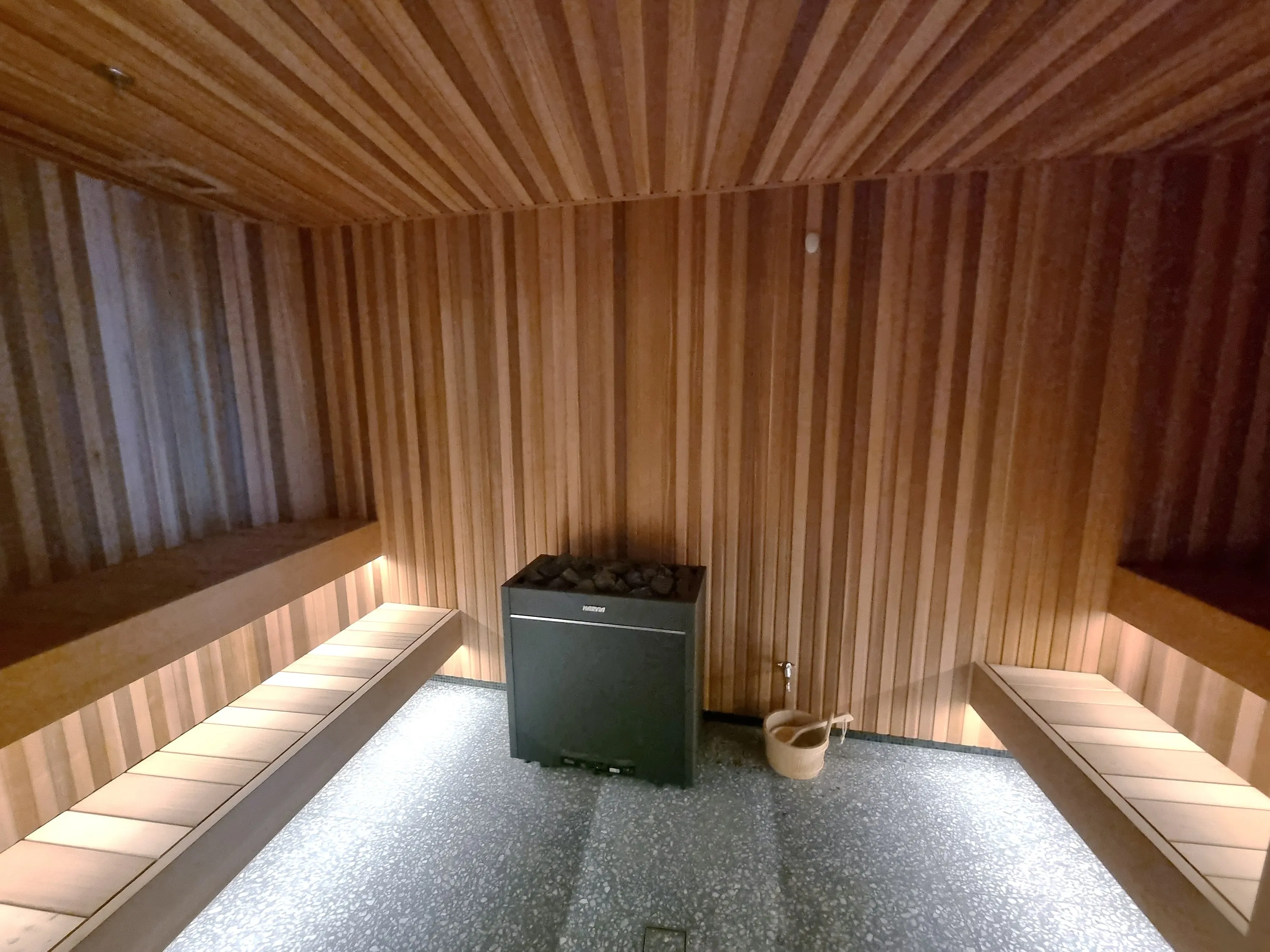 Timber-lined commercial sauna with lit benches on two sides and a black heater against the back wall