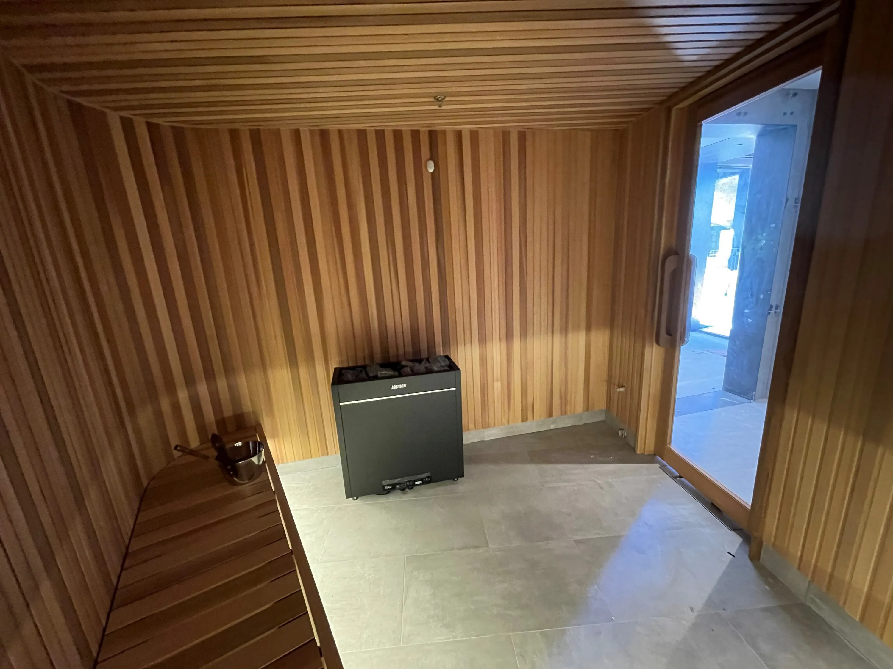 Floor-standing heater between a timber bench and a full-height glass sauna door
