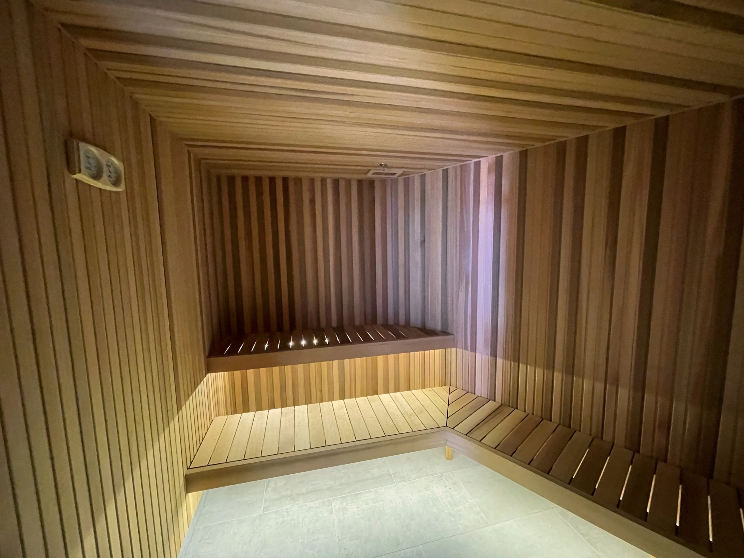Timber sauna with lit two-tier benches wrapping the corner beneath a timber ceiling