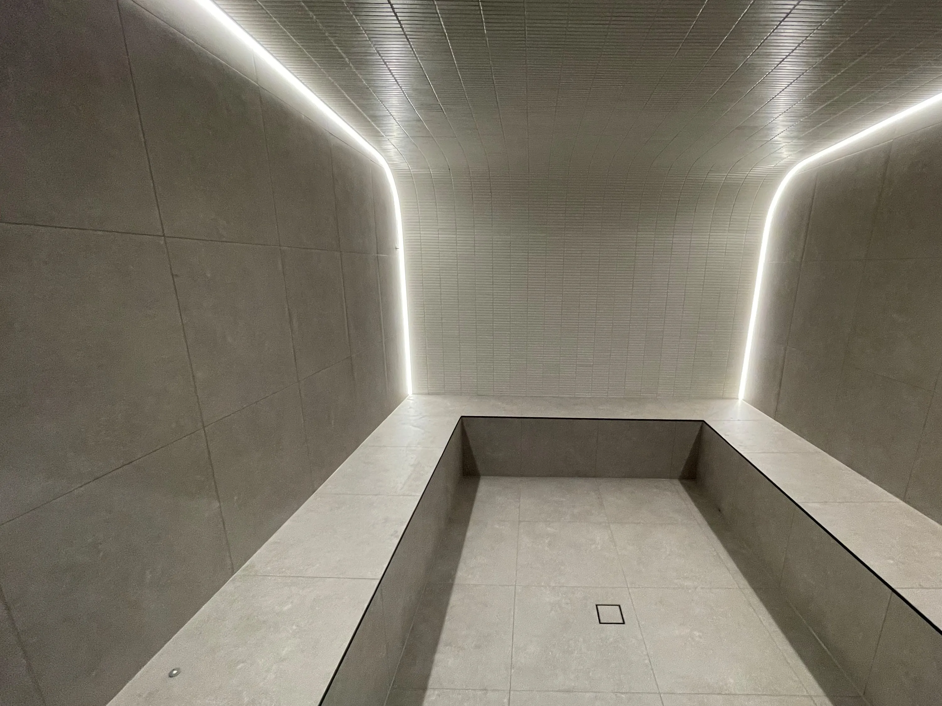 Commercial steam room with a vaulted ceiling outlined in soft linear lighting