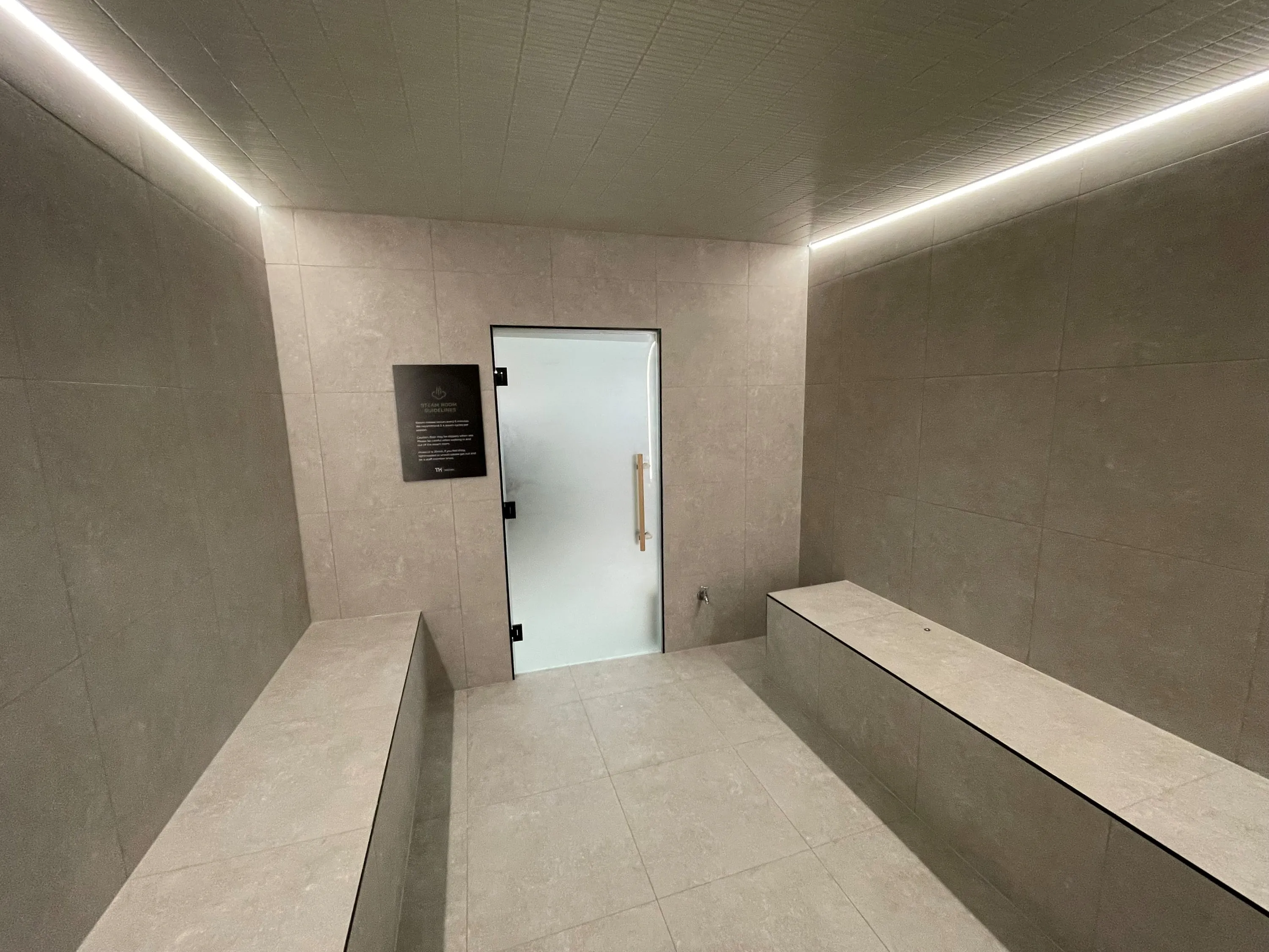 Tiled steam room with tiled benches on both sides, a frosted glass door and linear light along the ceiling