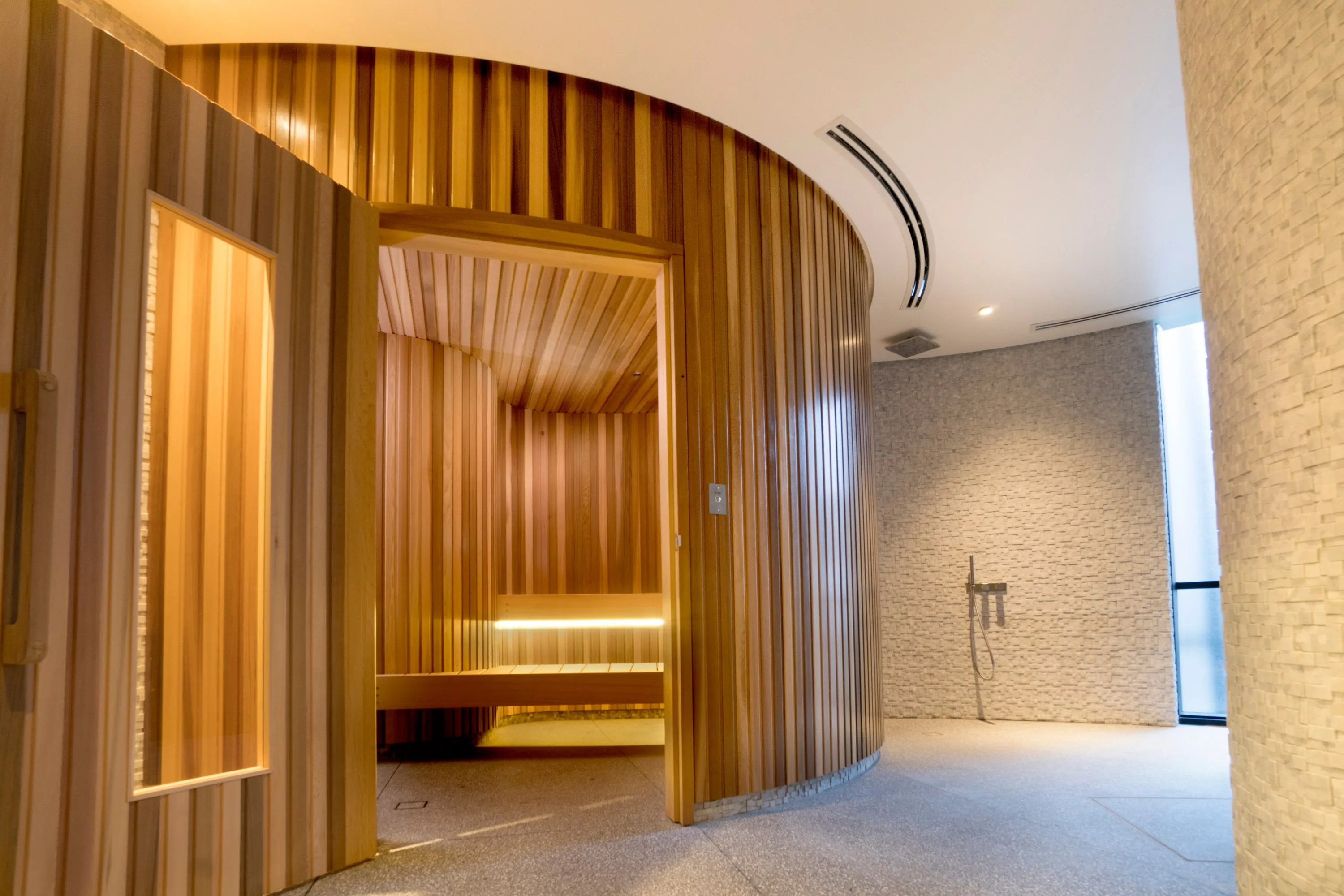 View into a curved cedar sauna with lit tiered benches