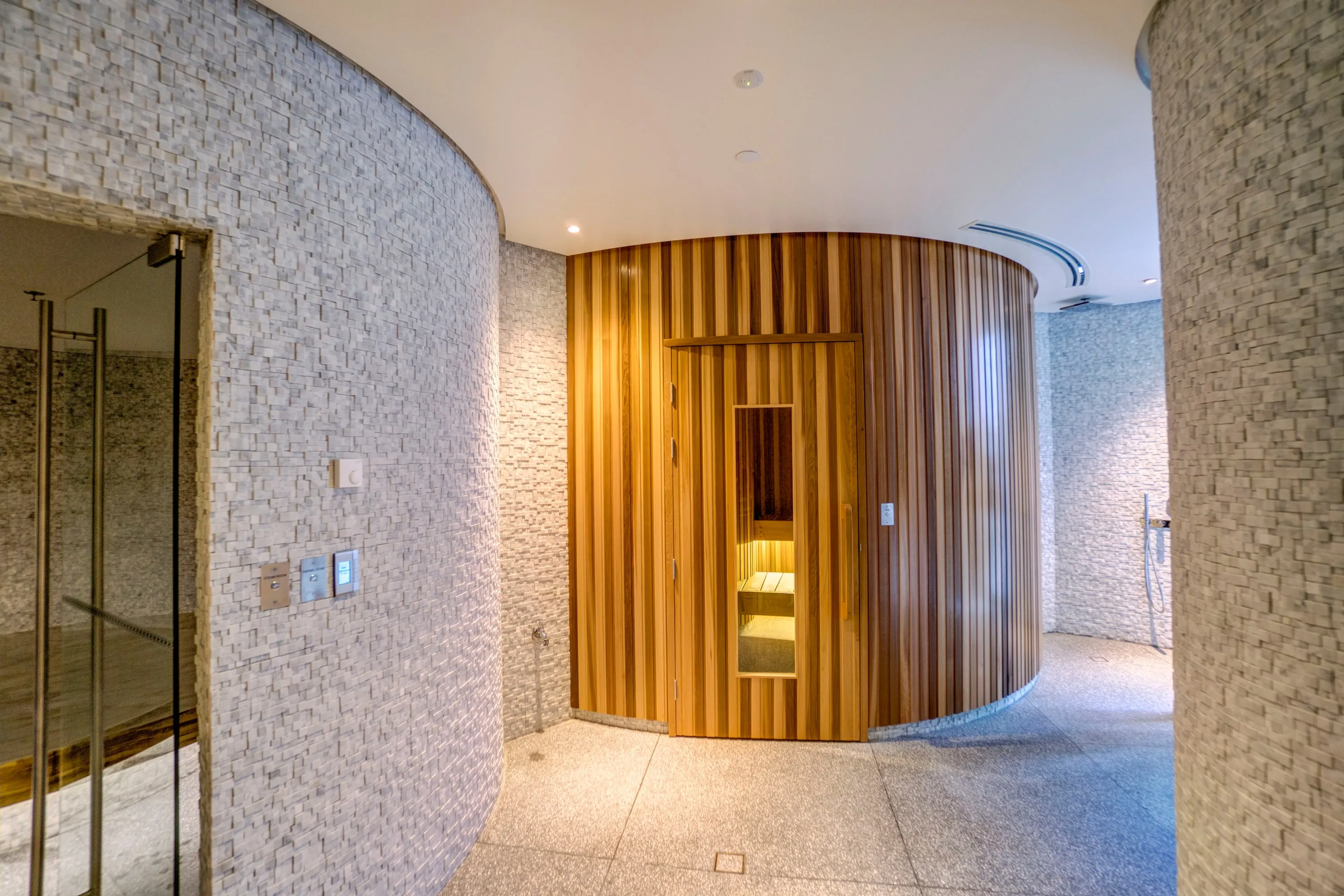 Curved cedar sauna pod in a stone wellness corridor