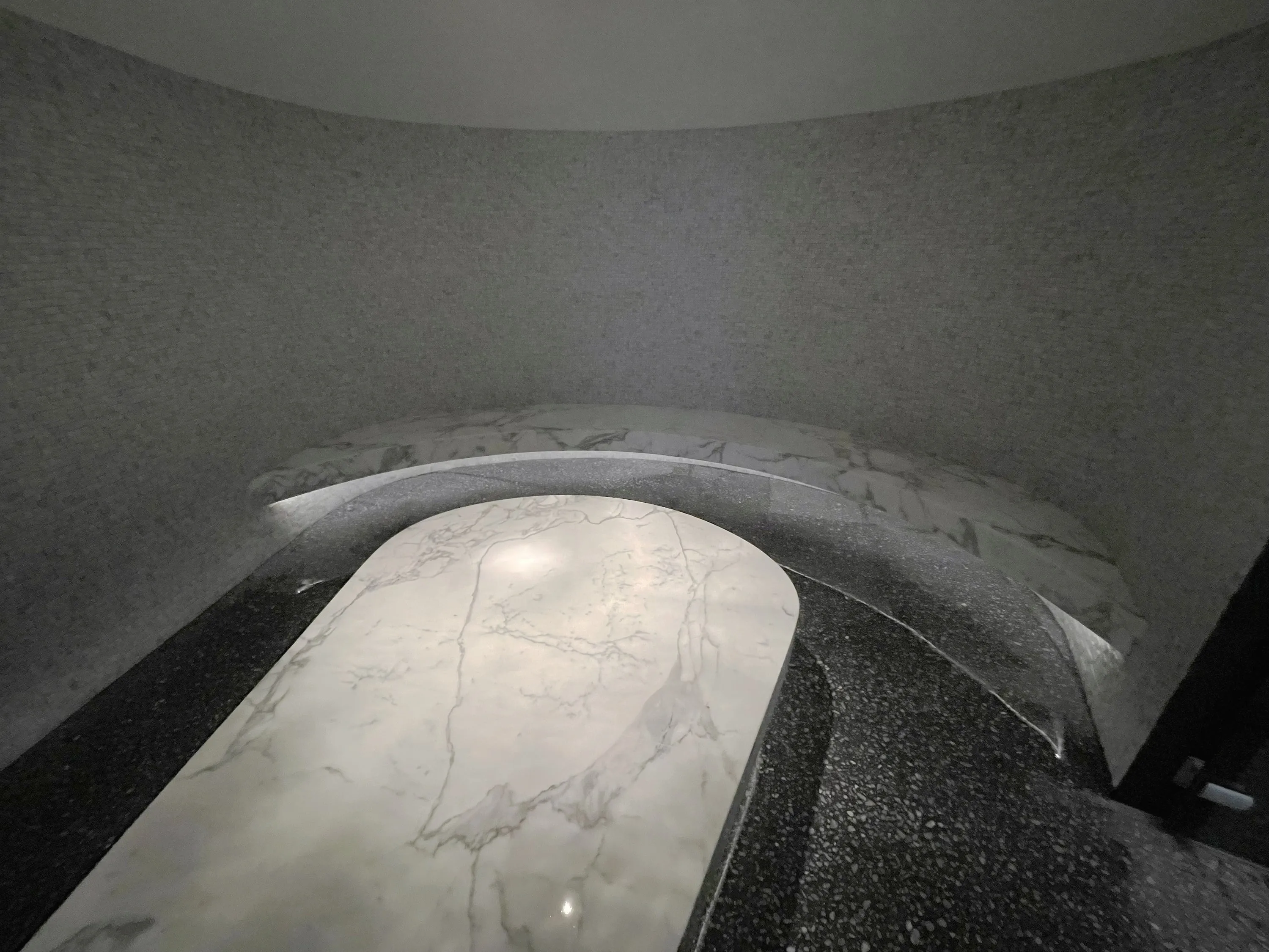 Curved steam room with a stone-topped island bench and a lit wall bench