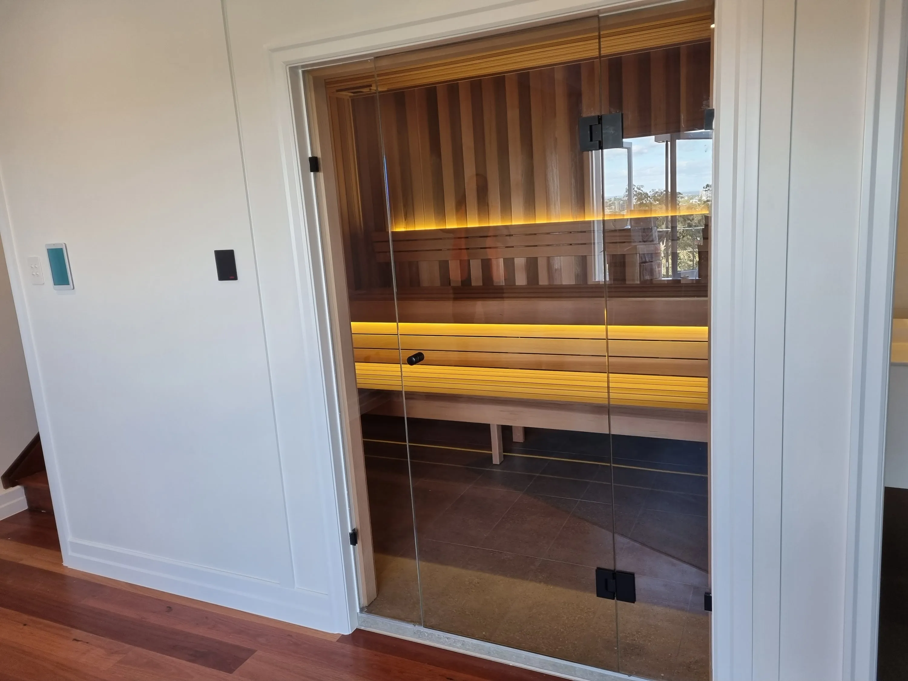 Frameless glass sauna front with glowing benches in a white-walled room