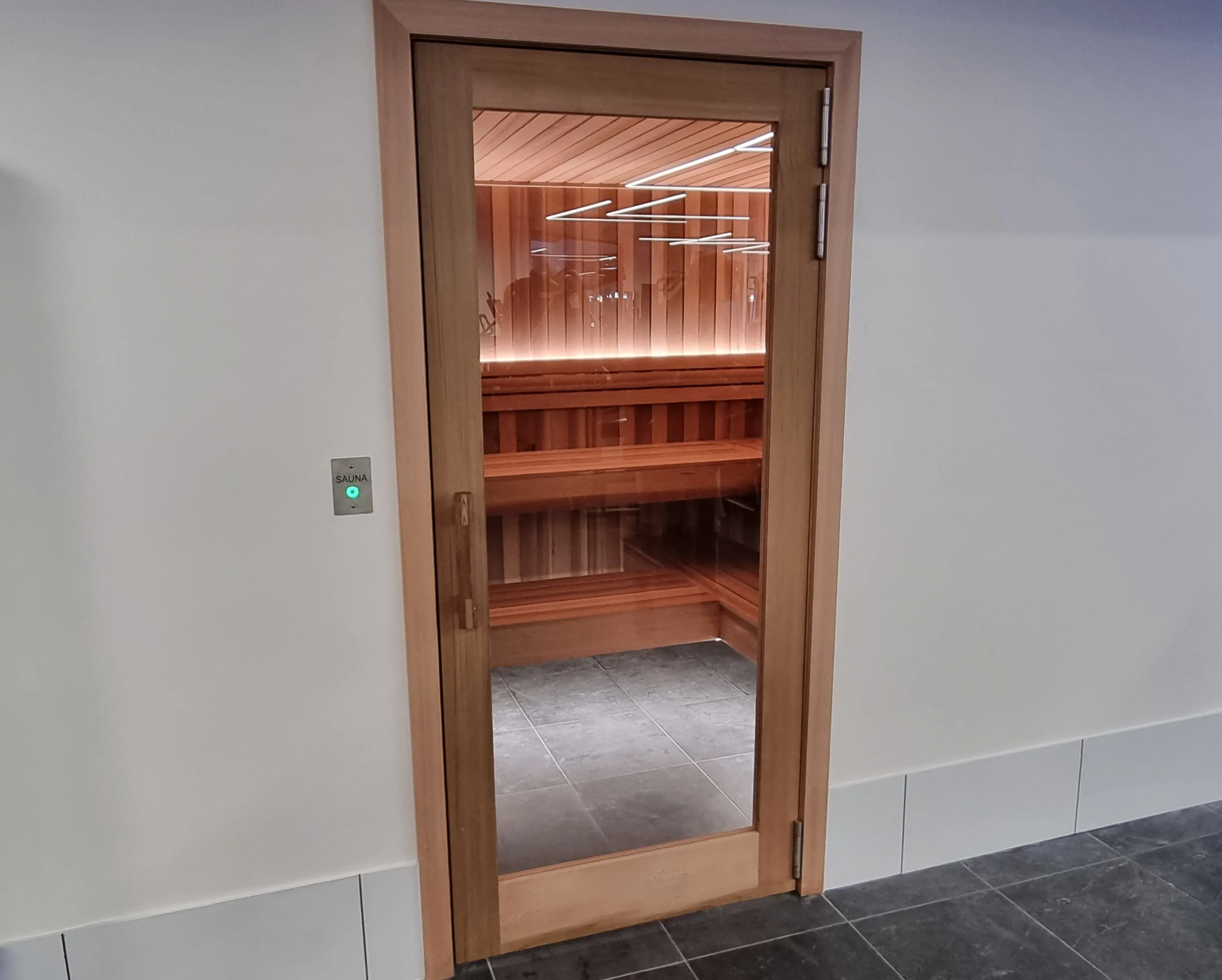 Timber-framed glass sauna door in a white gym wall