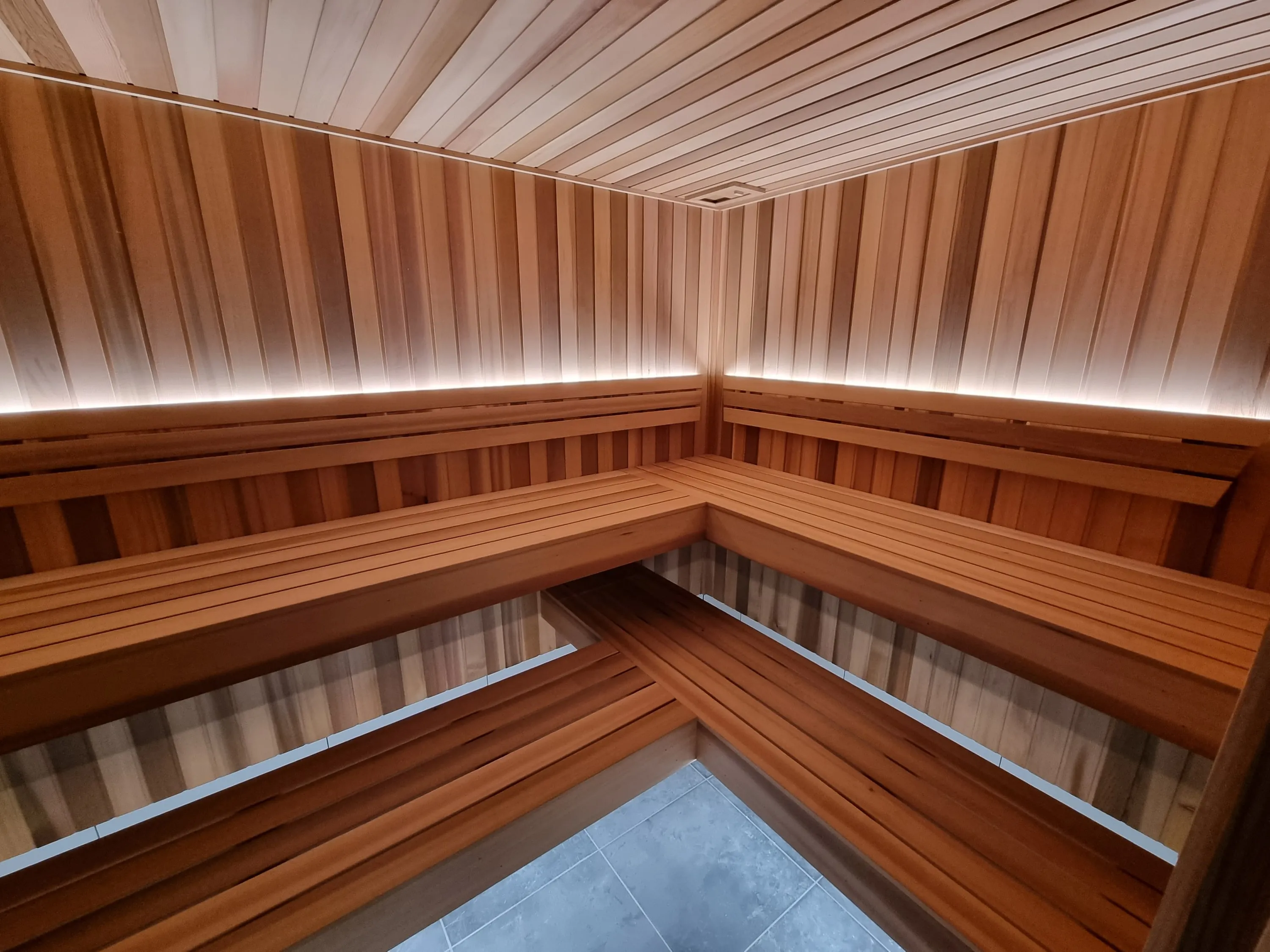 Timber gym sauna with two-tier L-shaped benches and soft strip lighting