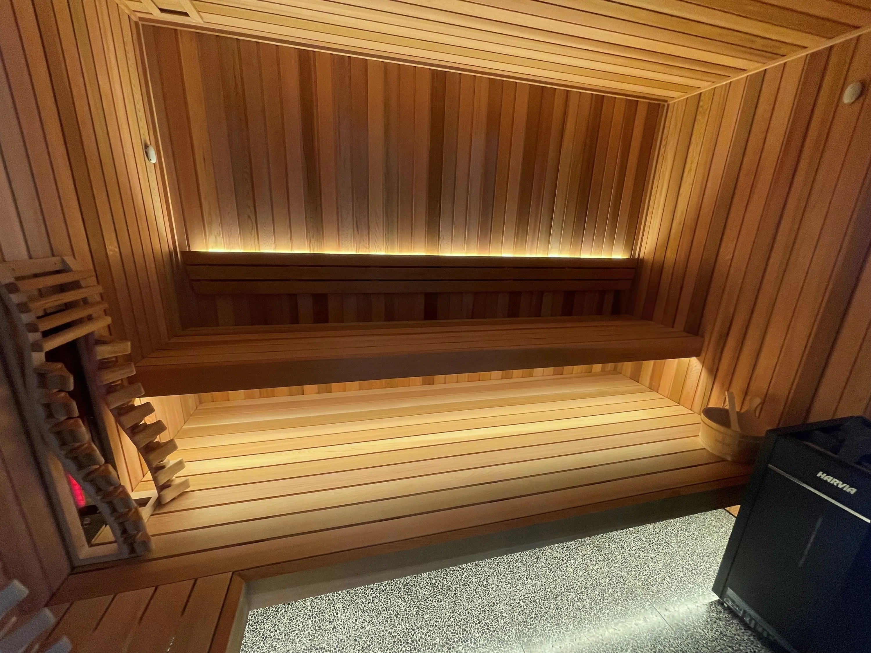Timber hybrid sauna with a stone heater and an infrared emitter behind a slatted guard, facing lit benches