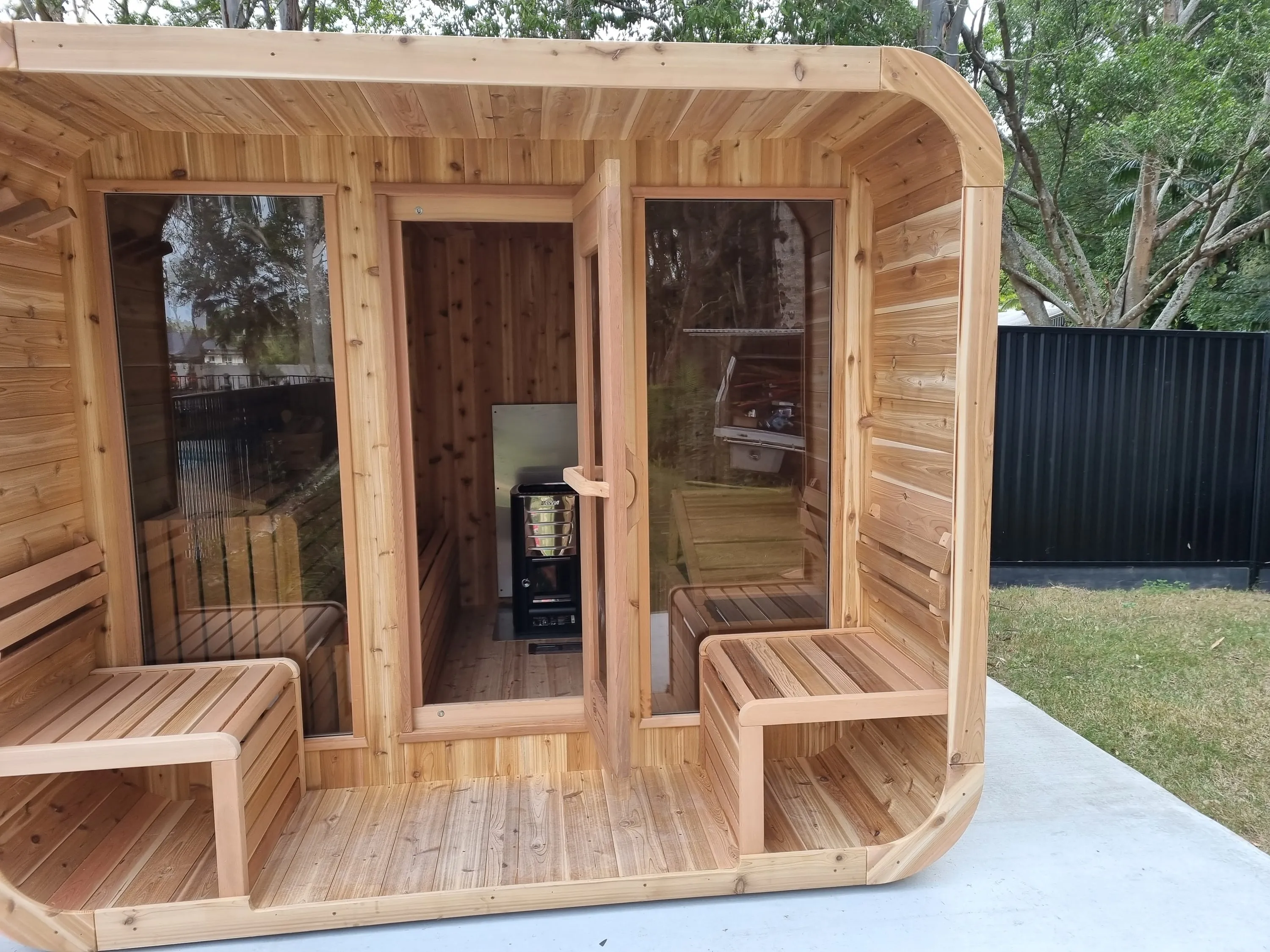 Rounded cedar Luna sauna with a glazed front and porch benches on a concrete pad