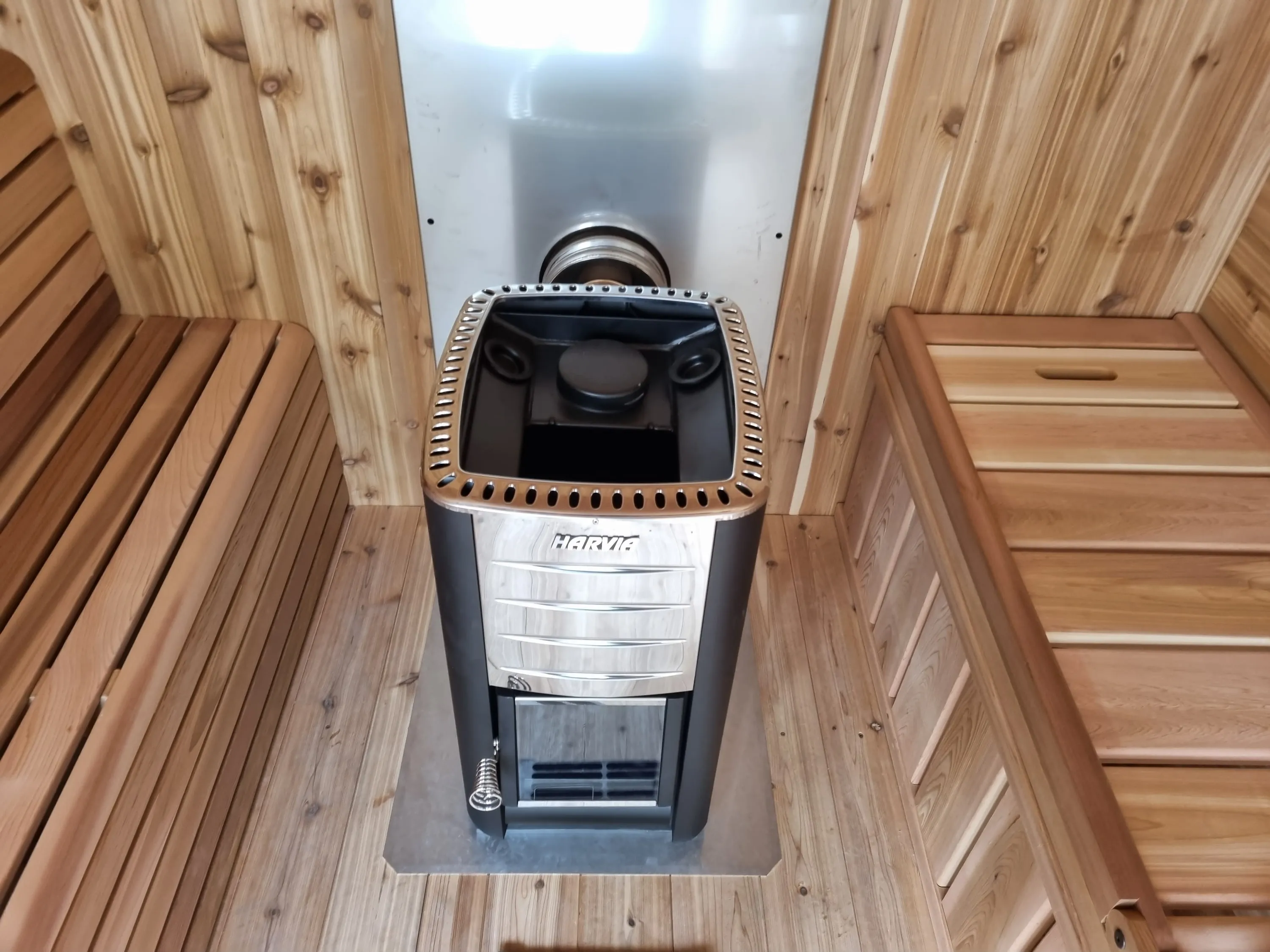 Wood-fired sauna heater in front of a metal heat shield inside the cedar sauna