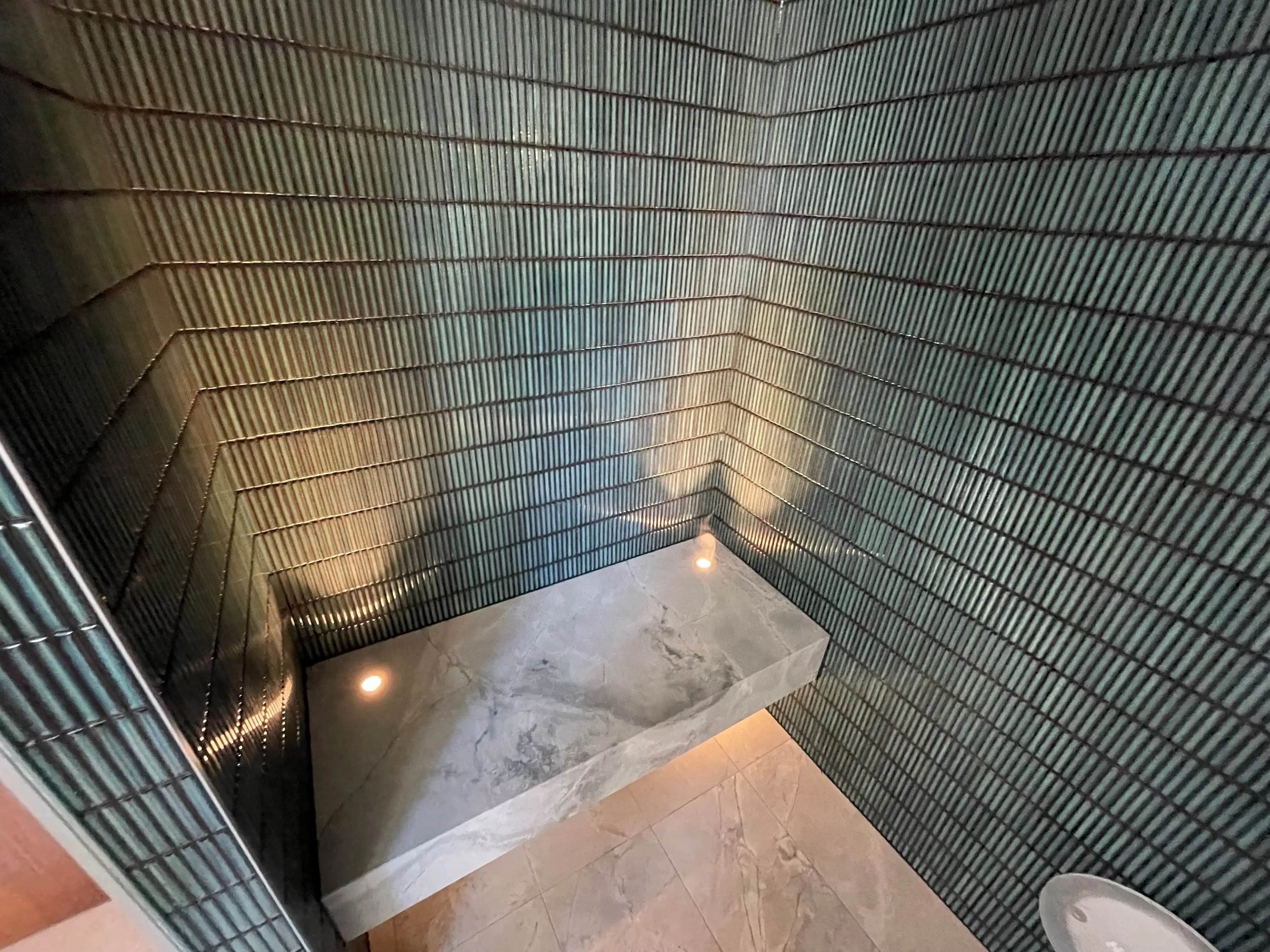 Steam room with green glazed tile walls and a floating stone bench lit from below