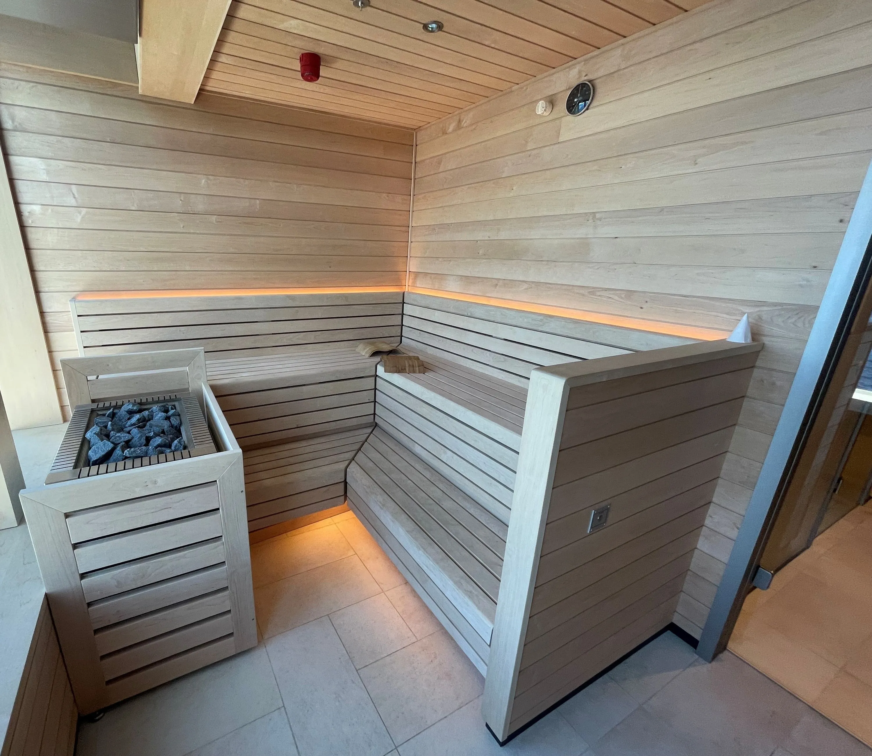 Commercial sauna with pale timber benches, a stone-filled heater and a window