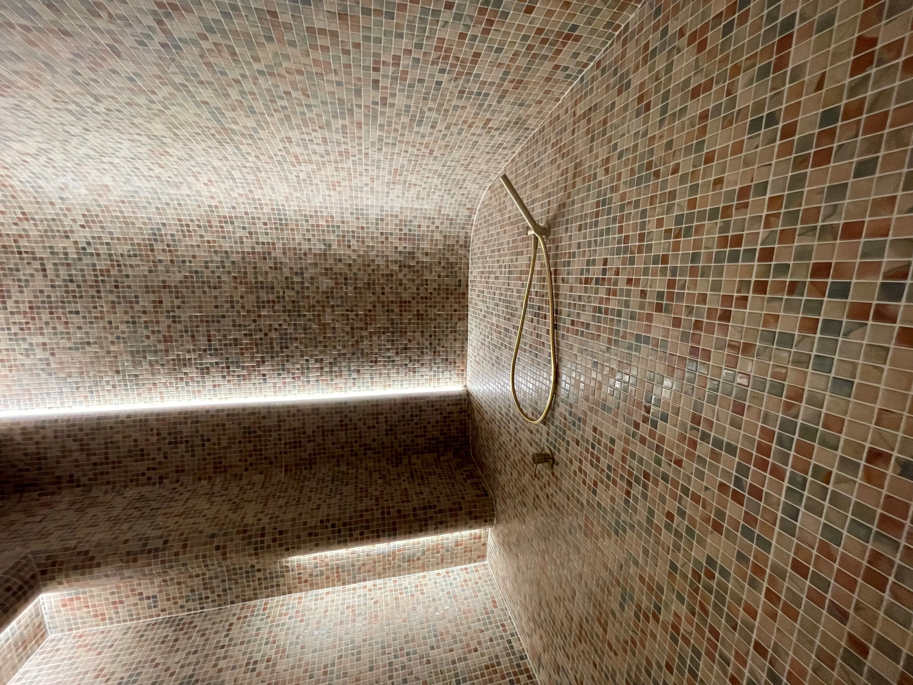 Mosaic-tiled steam room with a curved bench and soft lighting beneath the seat