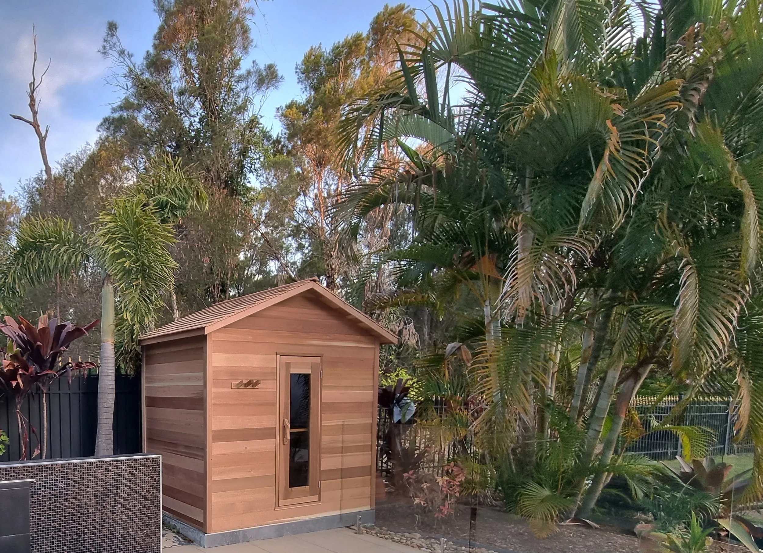 Gabled timber cabin sauna at the end of a pool terrace among palms