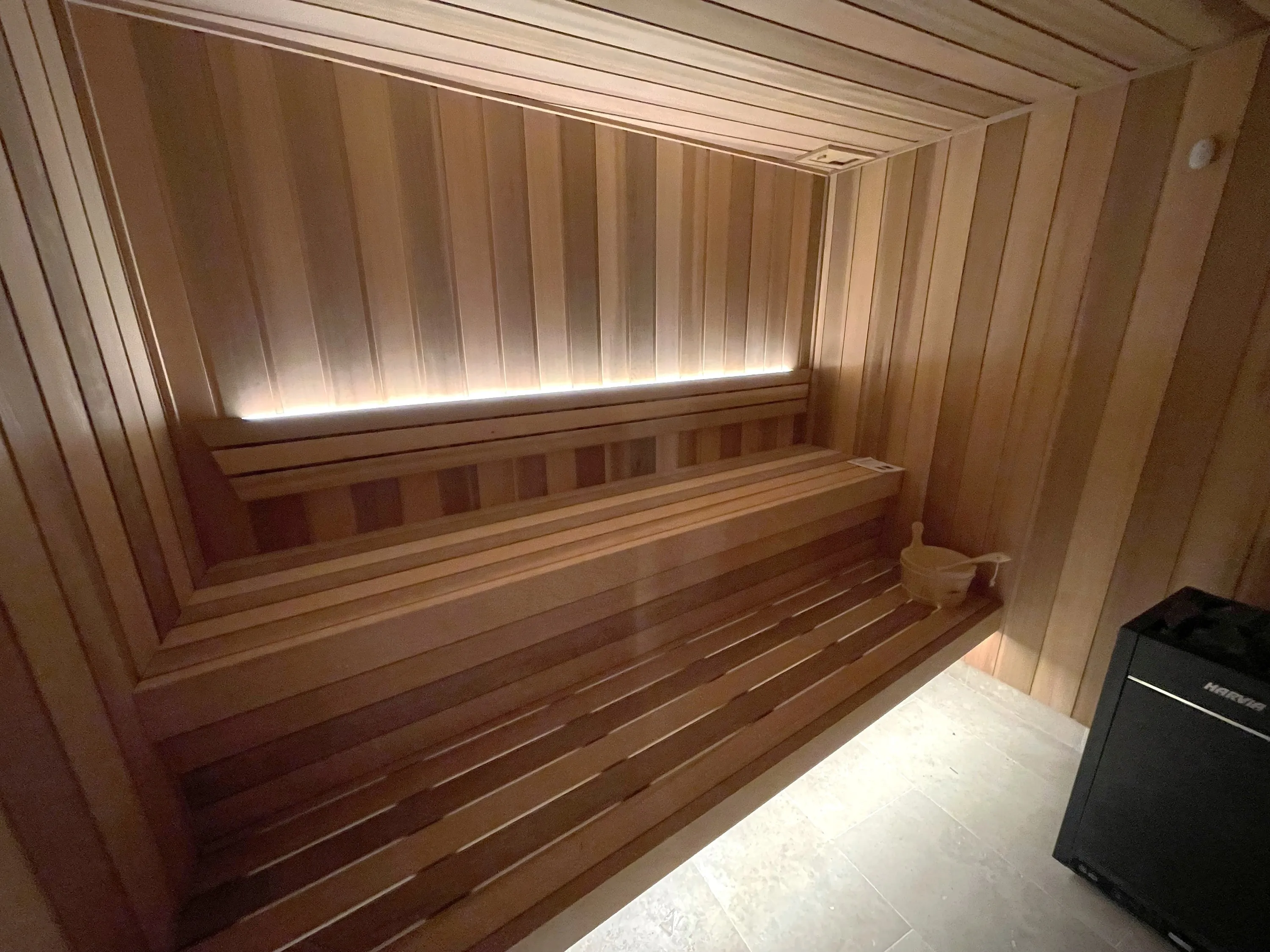 Warmly lit timber sauna with long benches and a floor-standing heater