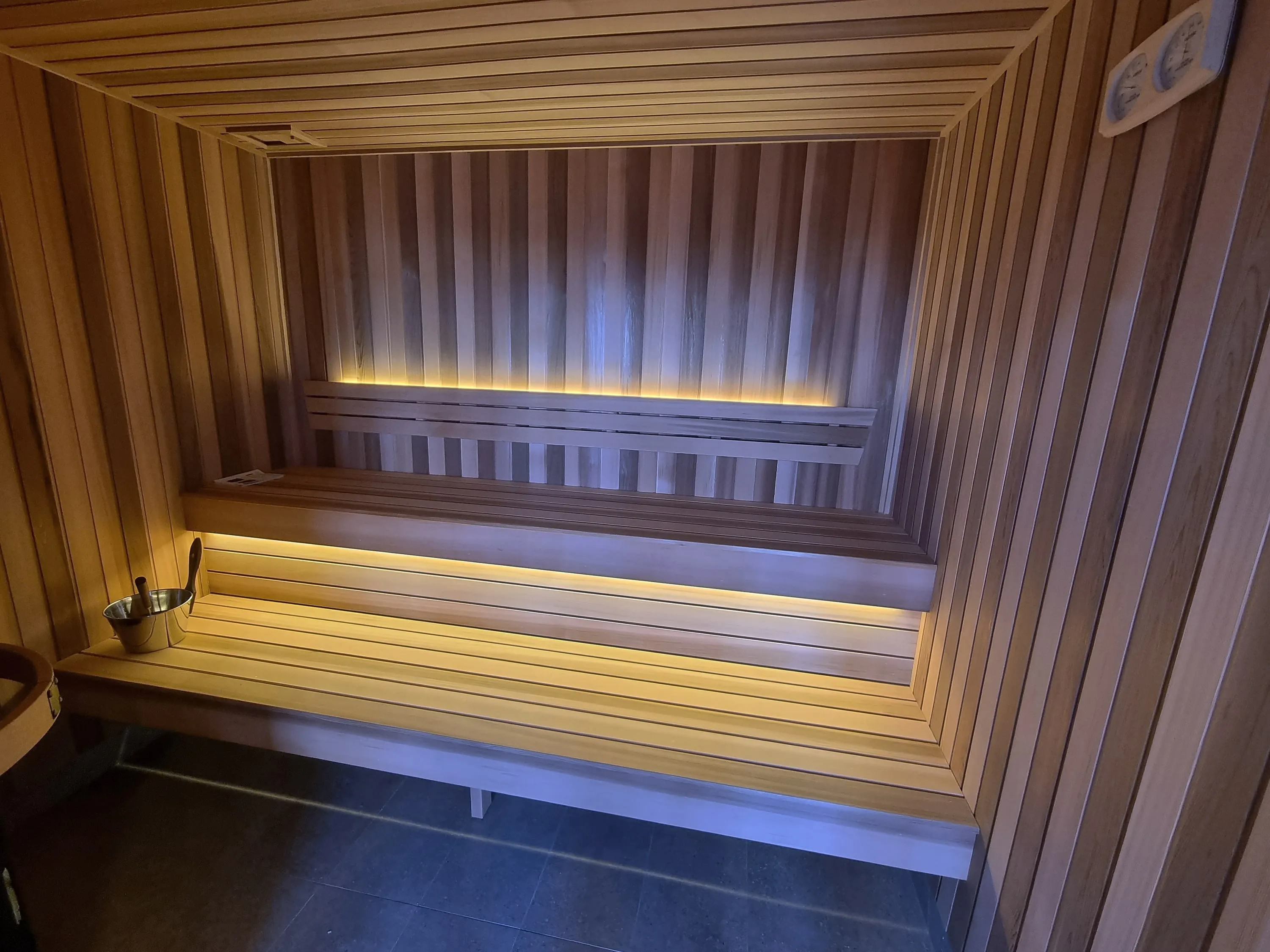 Timber home sauna with lit bench tiers and a frameless glass front