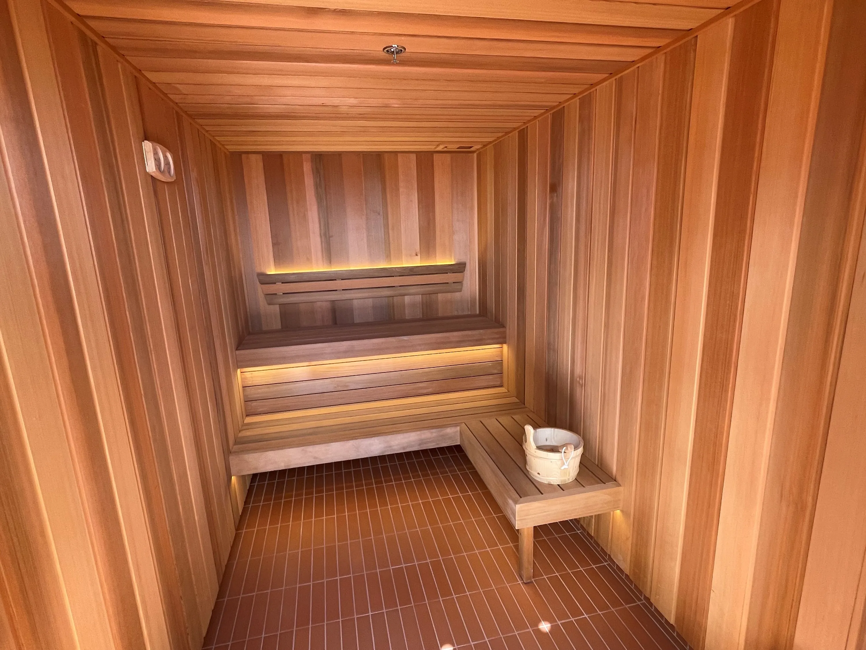 Timber sauna with two tiers of benches lit from beneath and a timber bucket on the lower bench