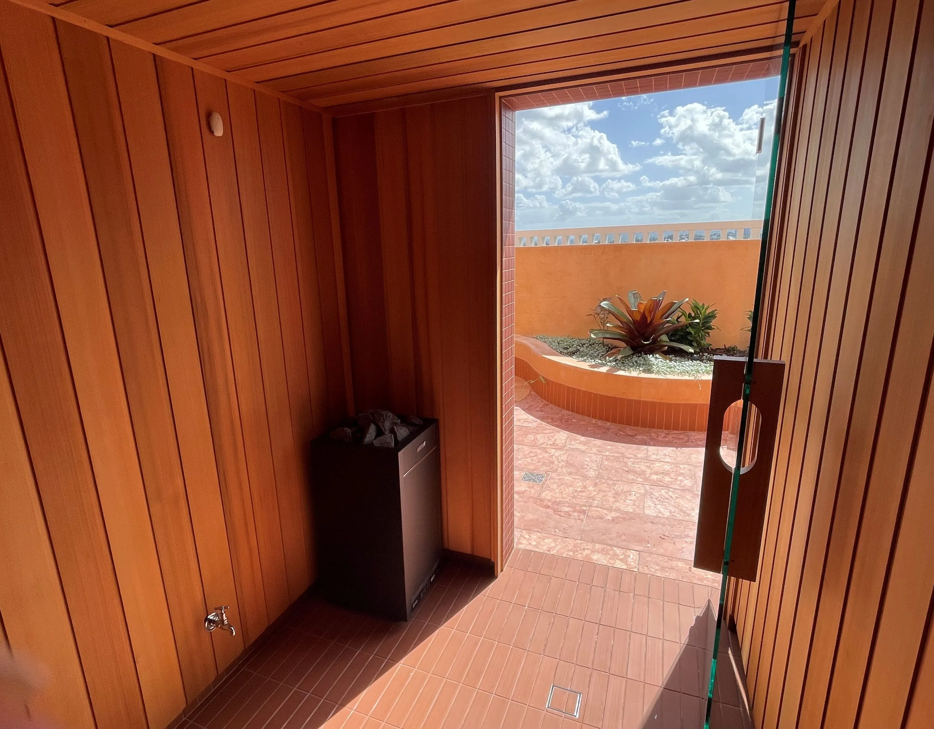 Timber sauna with its door open to a rooftop terrace and sky