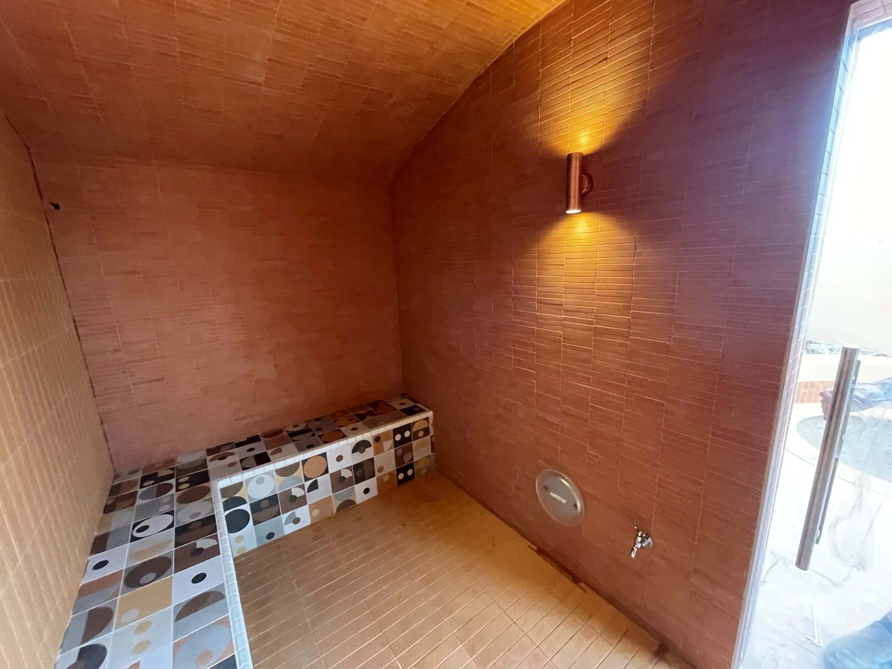 Tiled steam room with a copper wall light and an L-shaped bench in patterned tile