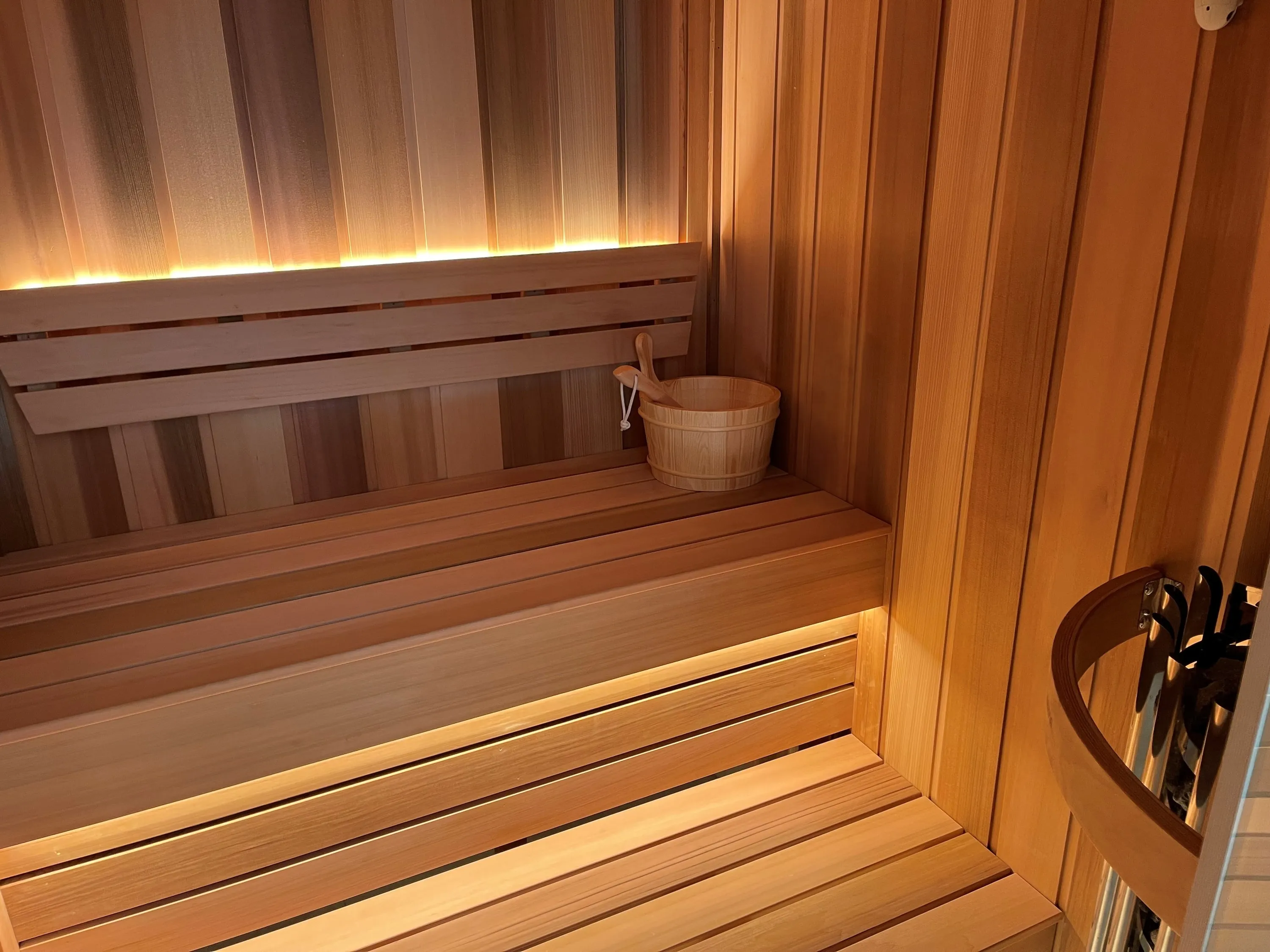 Lit timber backrest and bench with a sauna bucket and ladle