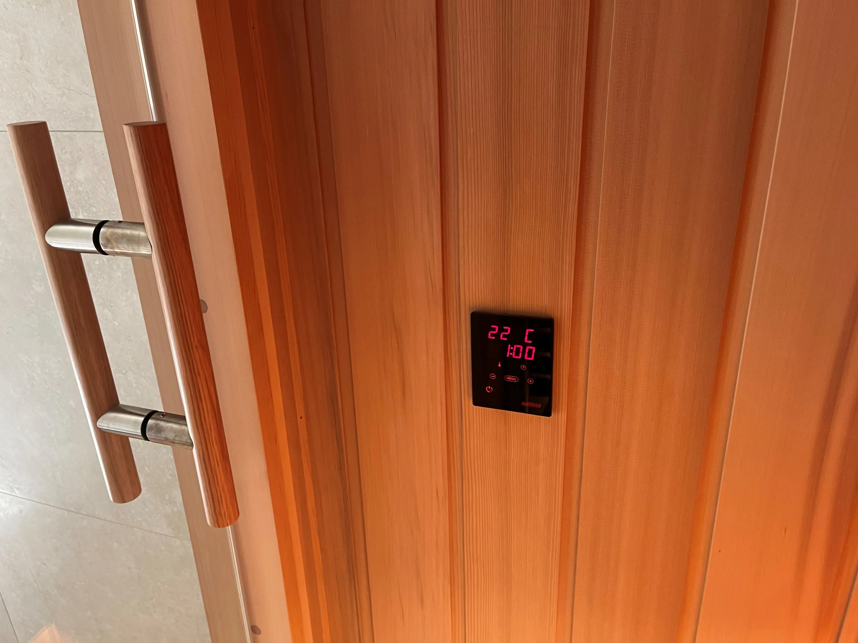 Digital sauna control panel set into timber beside the door handle