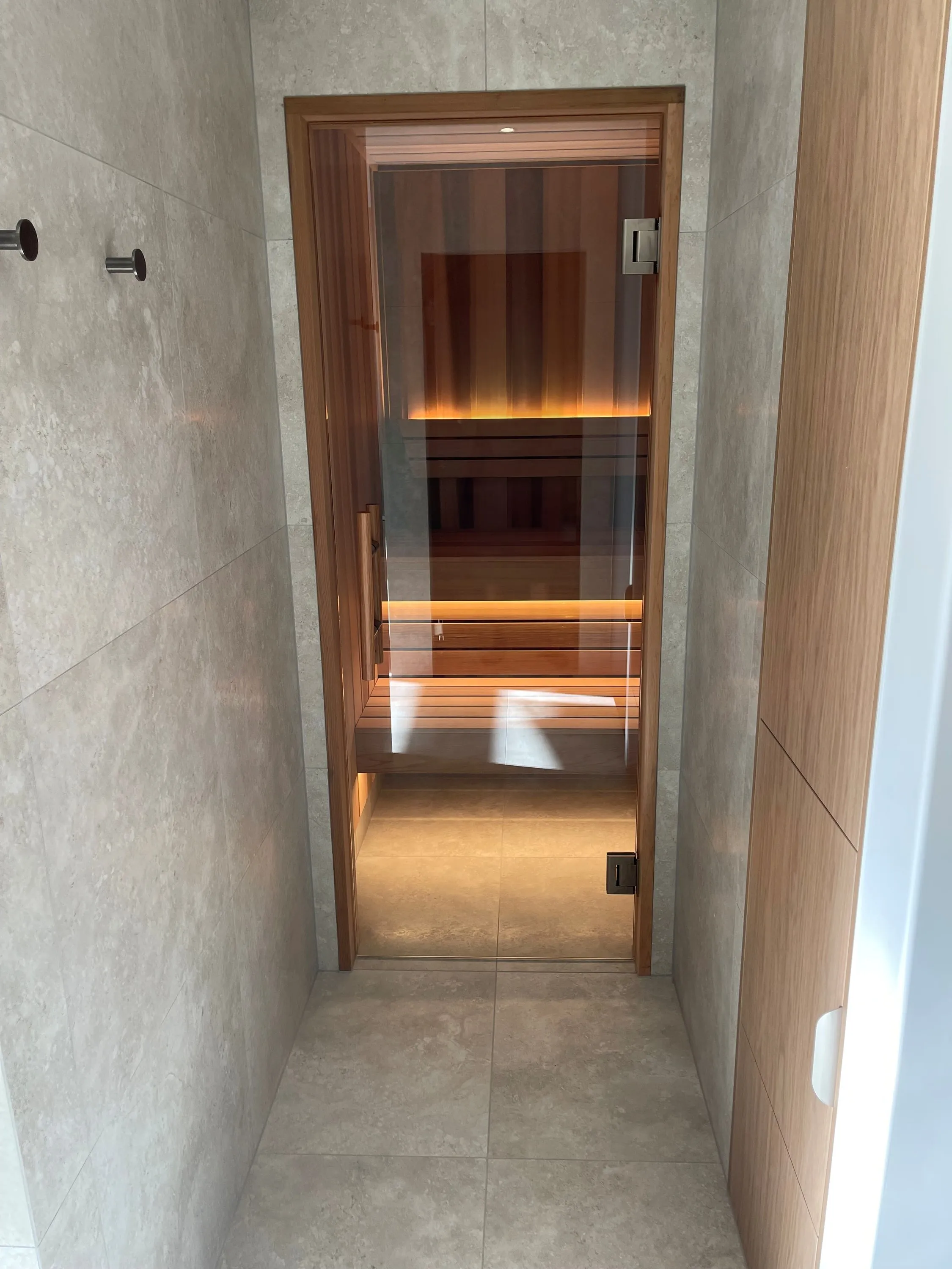 Frameless glass sauna door at the end of a tiled bathroom