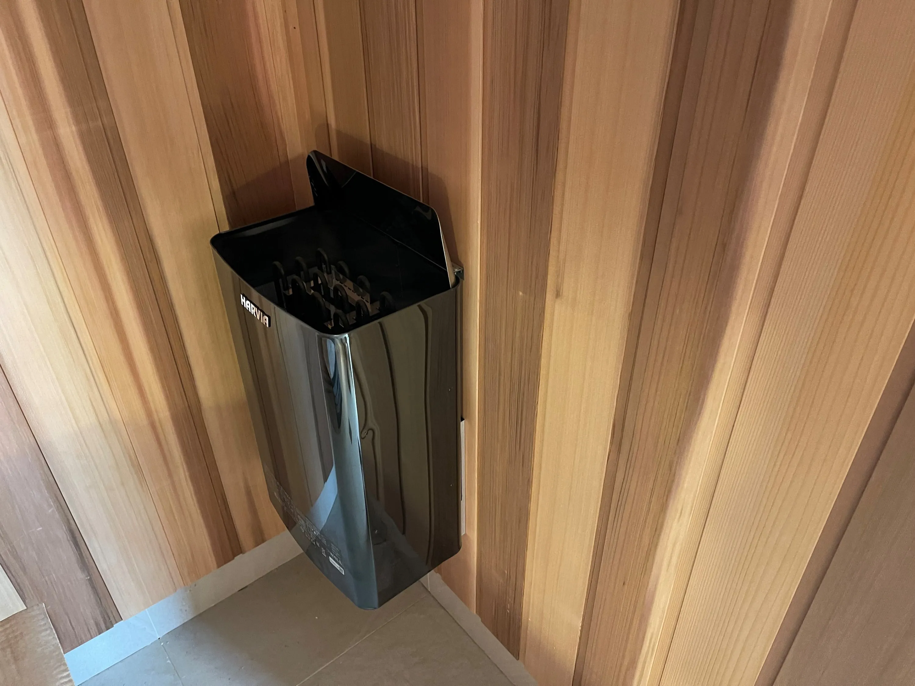 Black sauna heater filled with stones against a timber wall