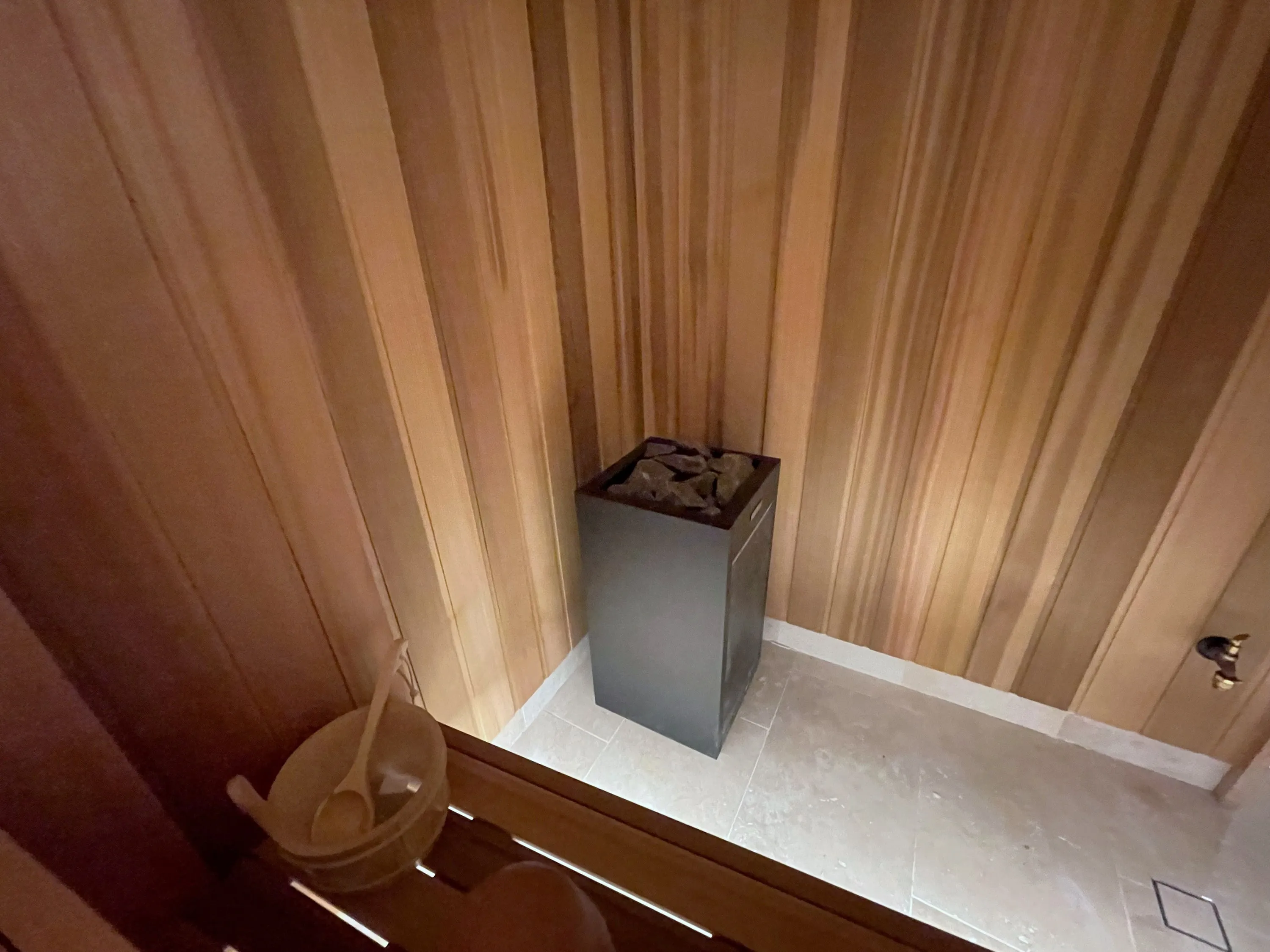 Floor-standing sauna heater with stones beside a timber bucket and ladle