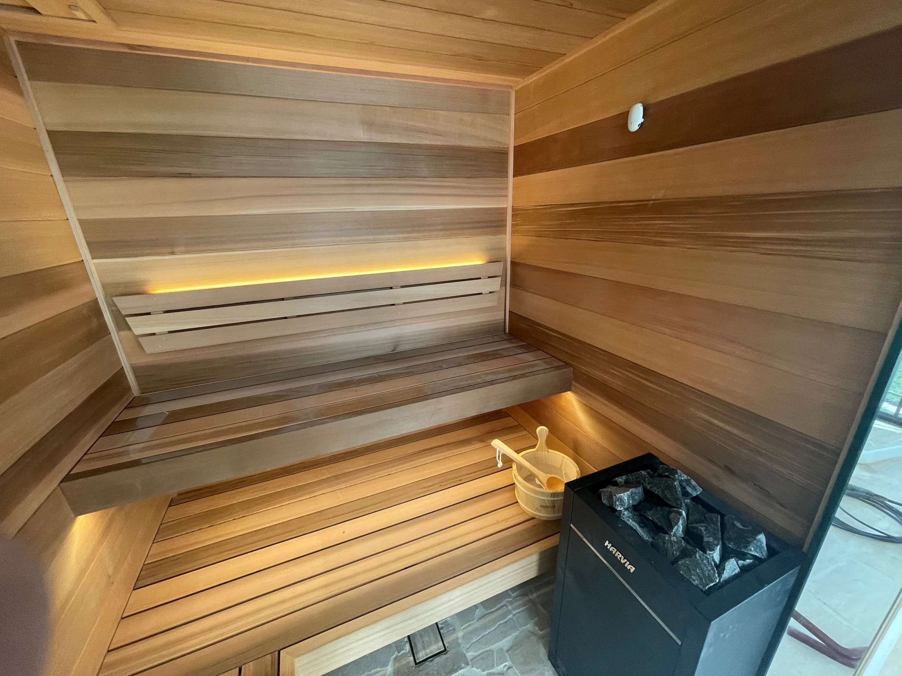 Floor-standing heater with stones in the corner of a lit timber sauna