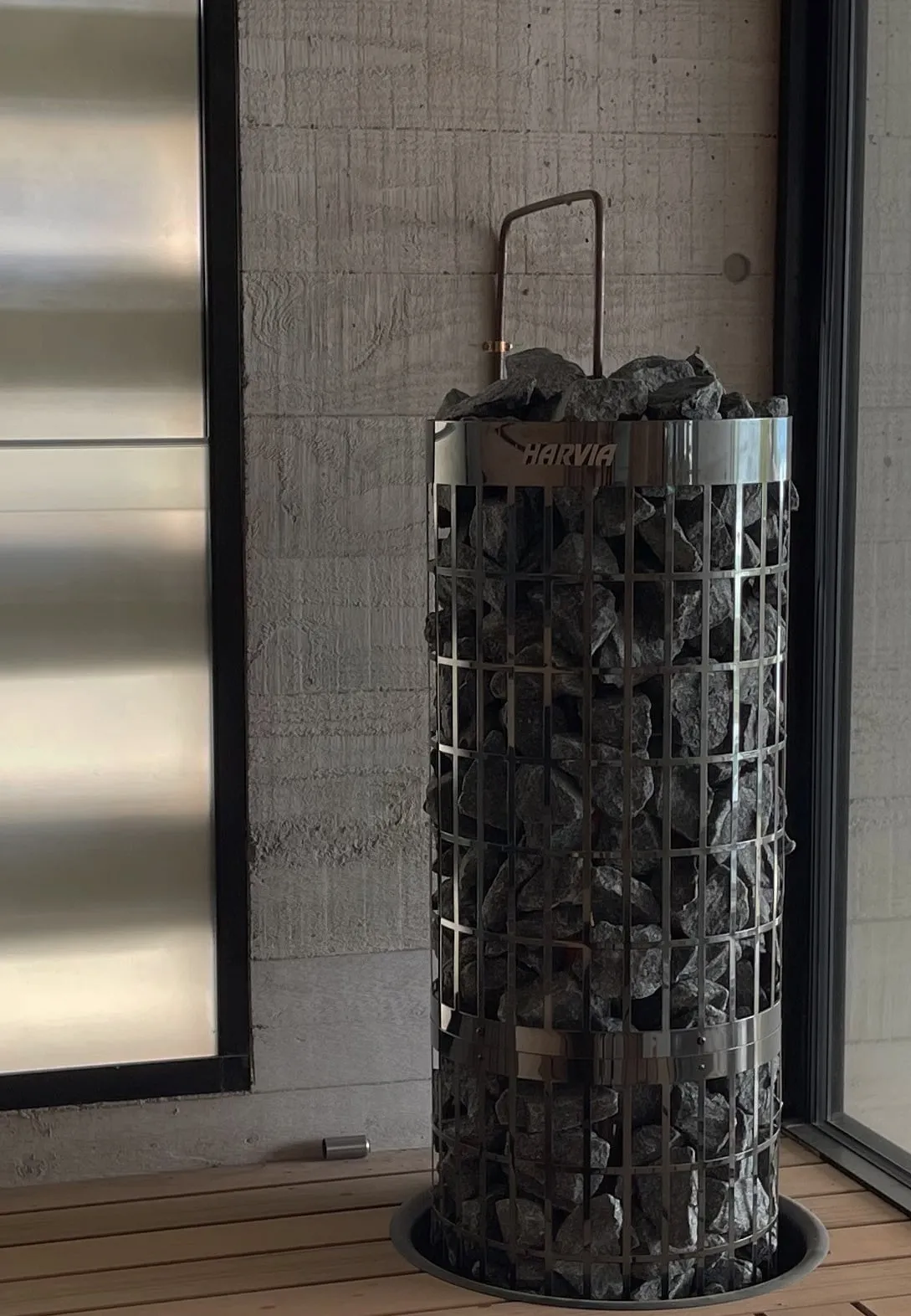 Tower heater filled with stones in its steel guard, against board-formed concrete