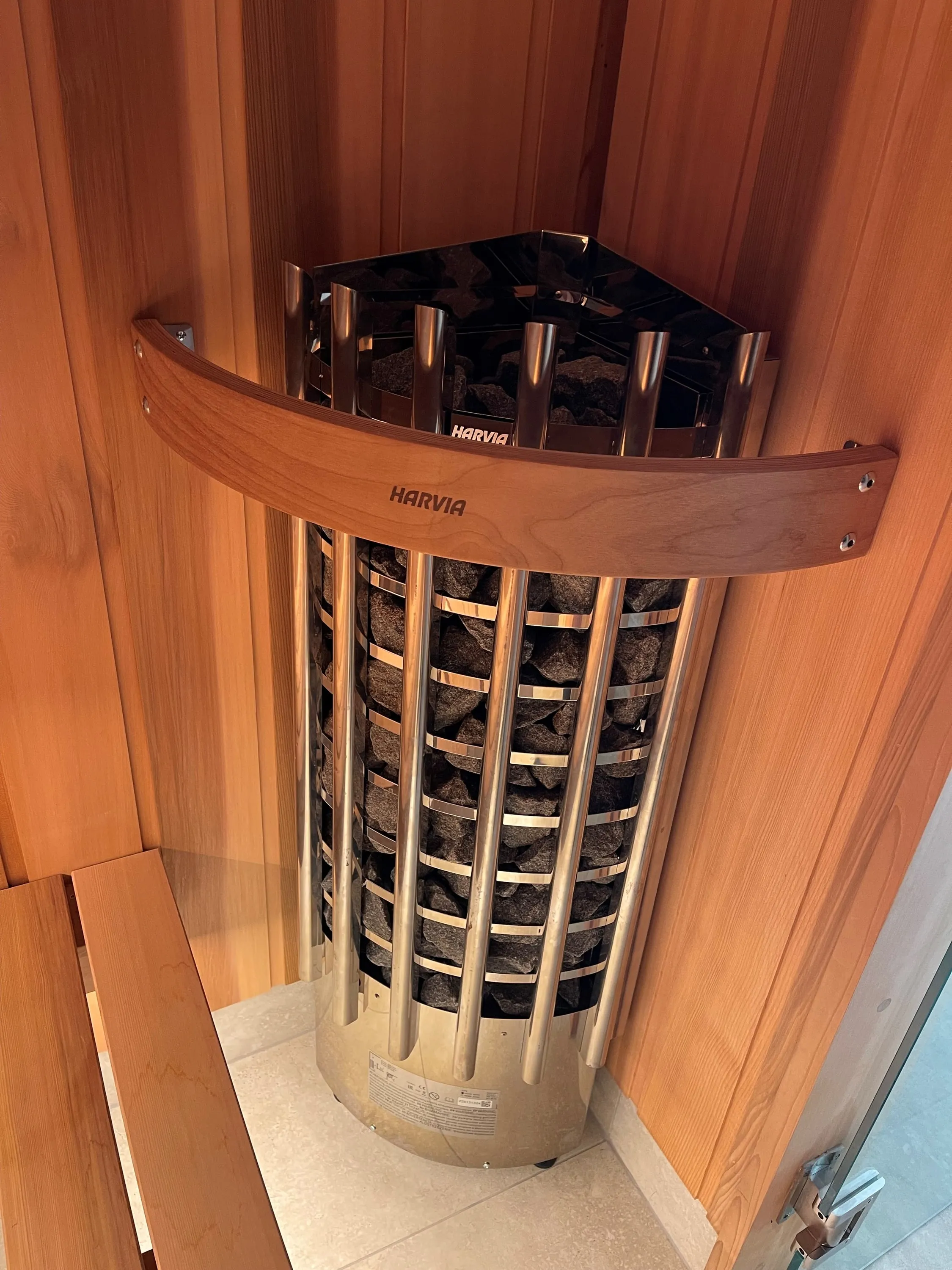 Tall cylindrical sauna heater filled with stones beside a timber bench