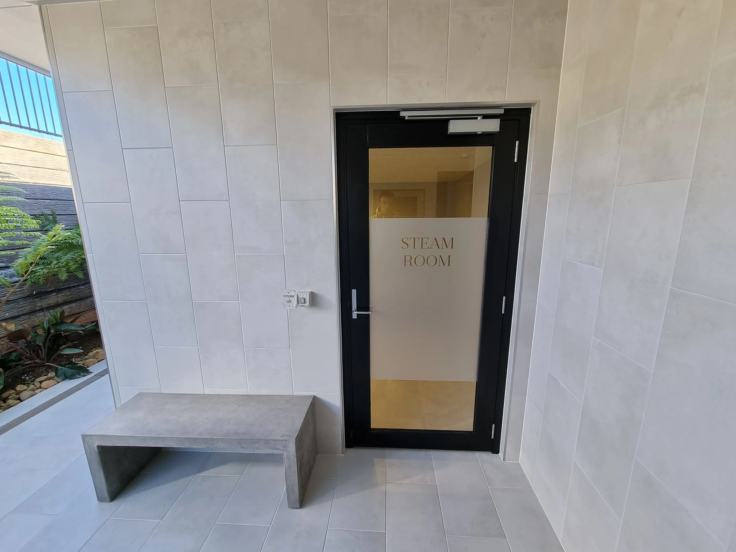 Black-framed glass steam room door beside a tiled bench