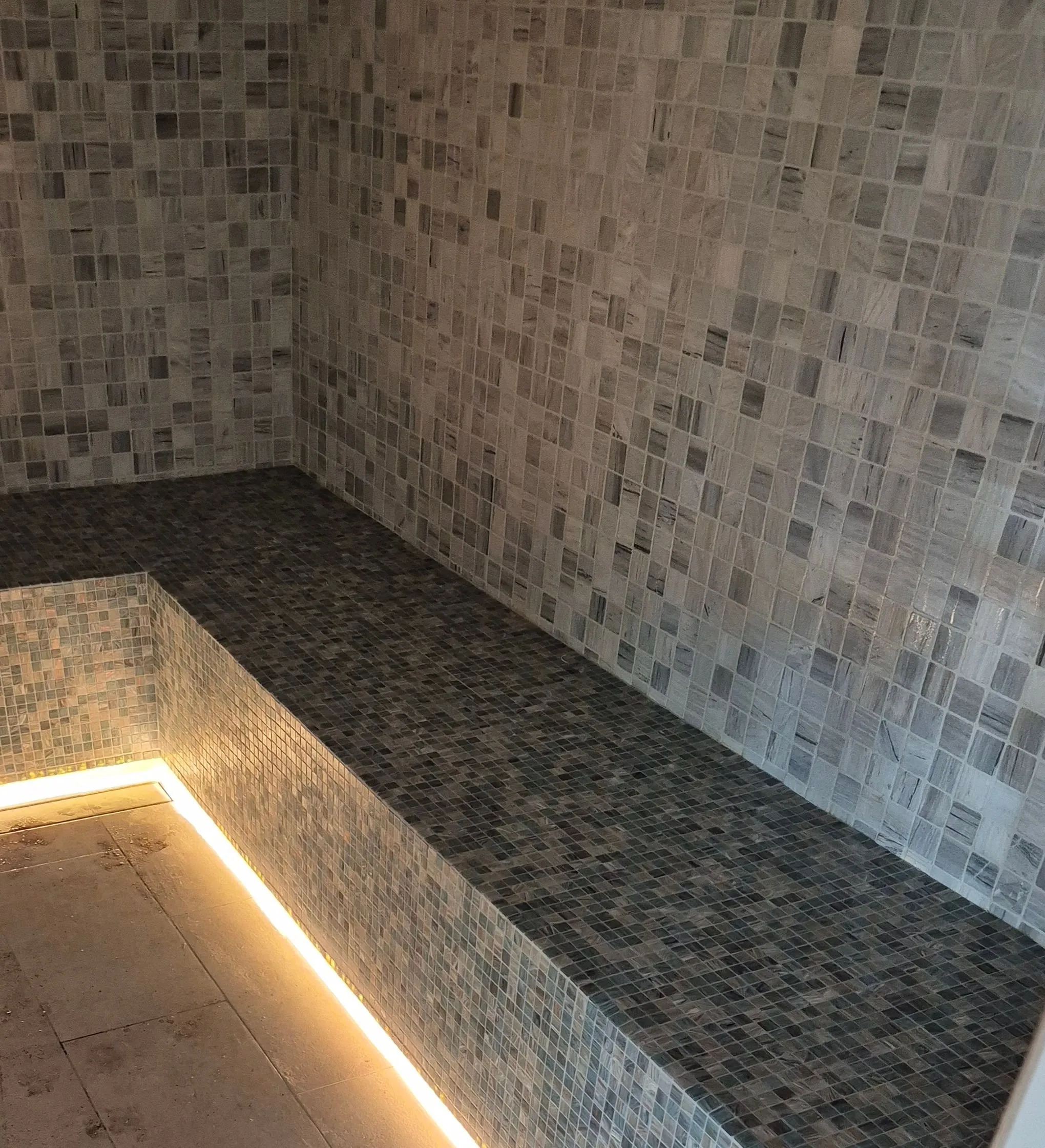 Continuous light line beneath a mosaic-tiled steam room bench