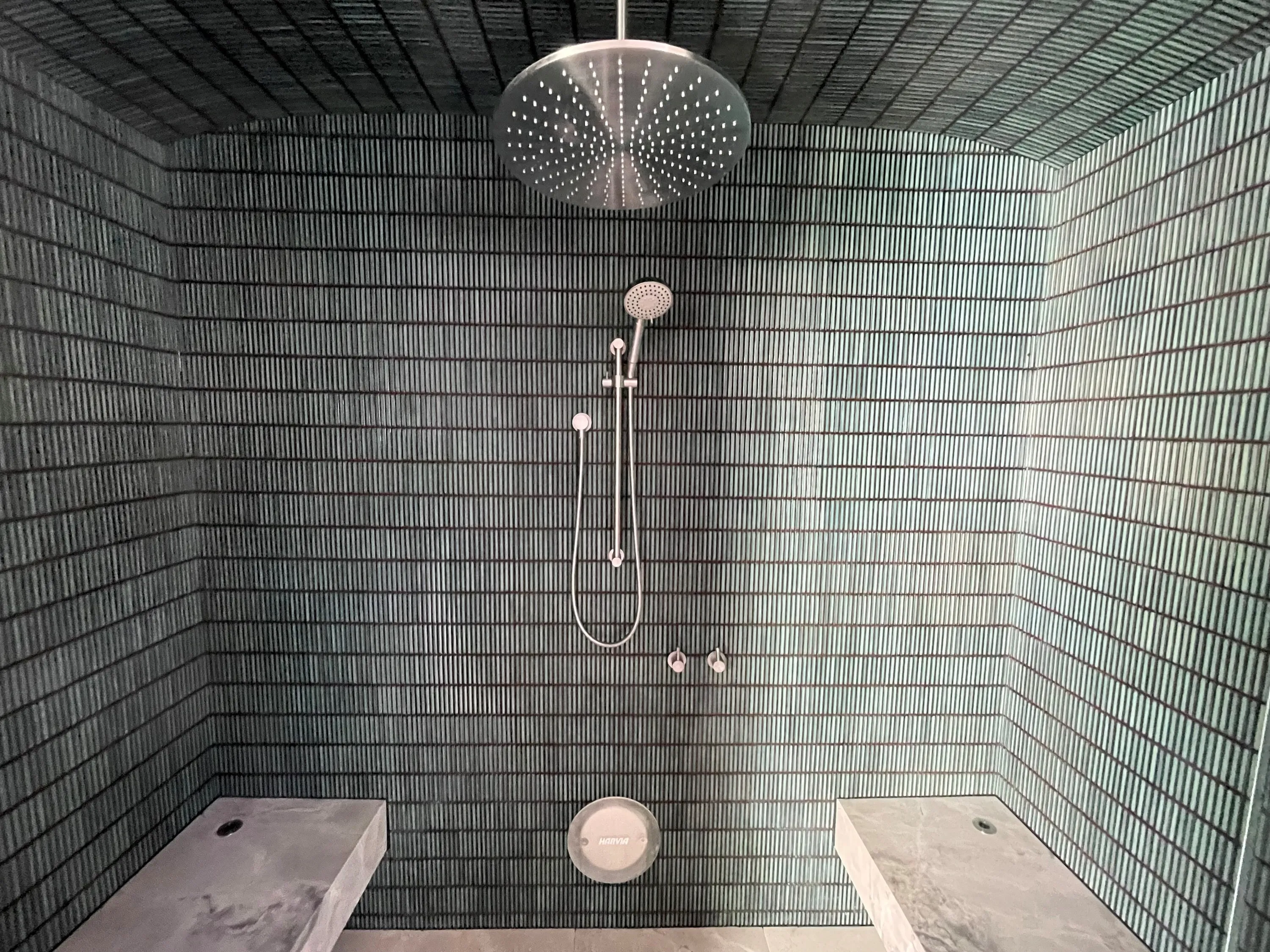 Steam room with green glazed tile walls and two floating stone benches