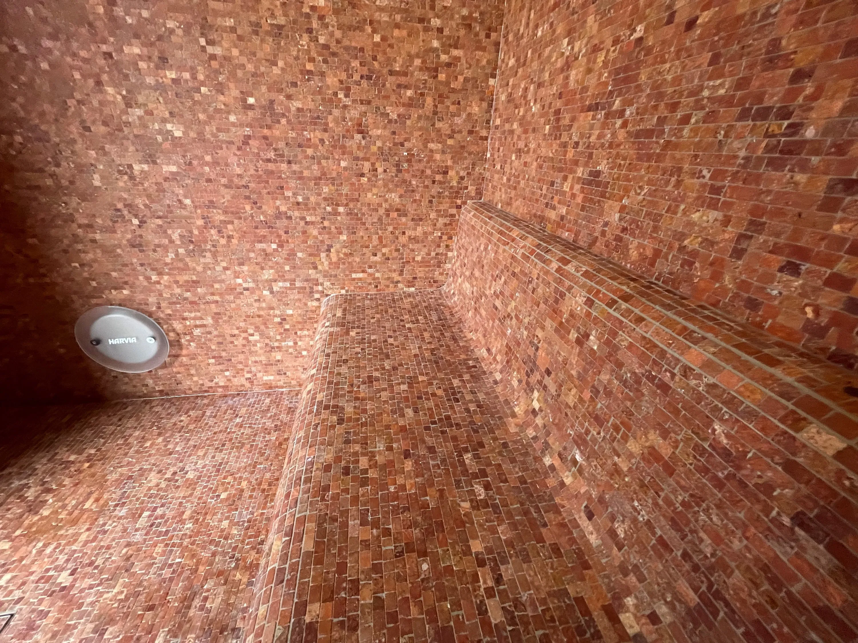 Steam room lined in warm terracotta mosaic with a curved, formed bench