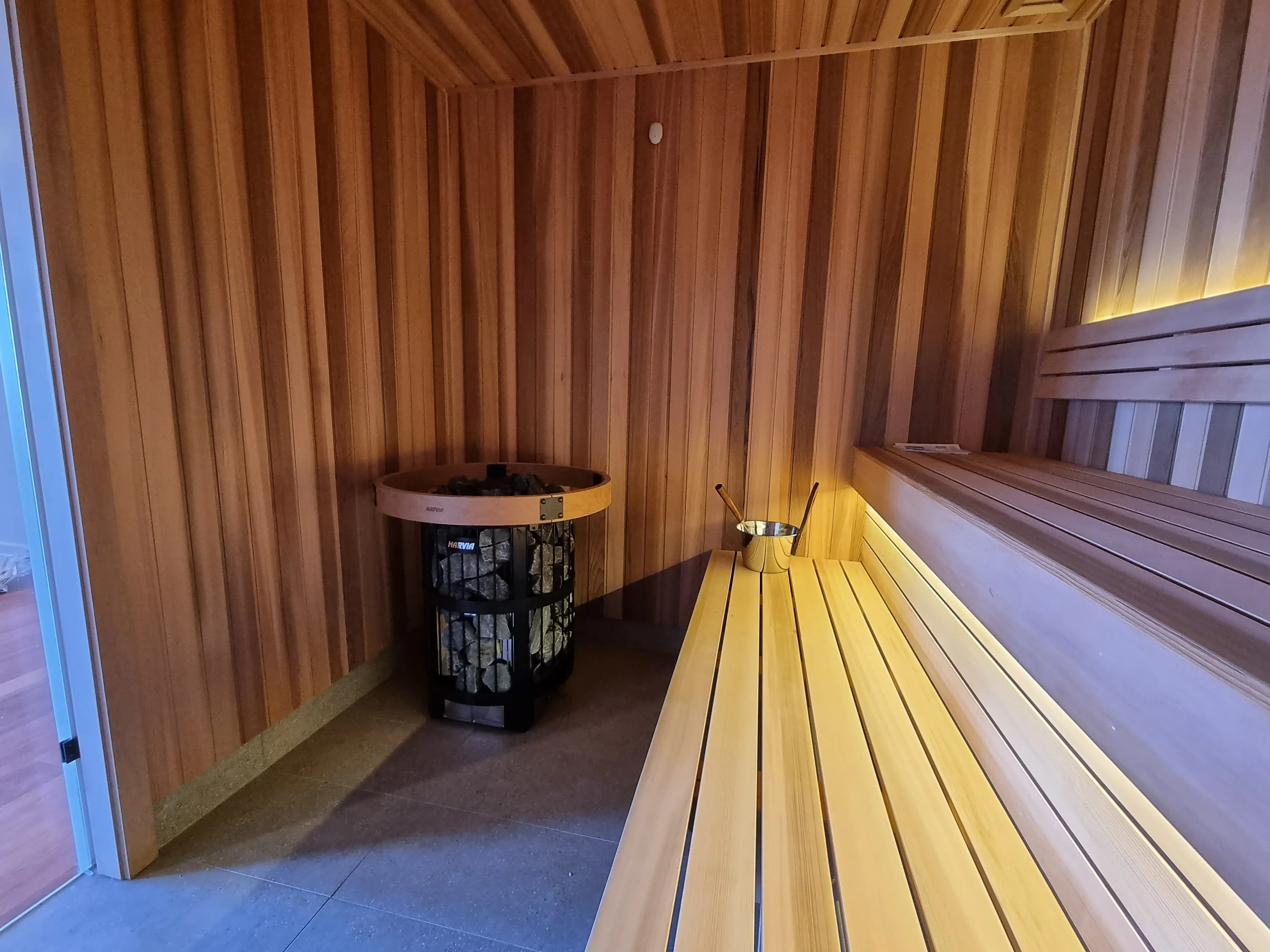 Round tower heater and lit timber bench along the sauna wall