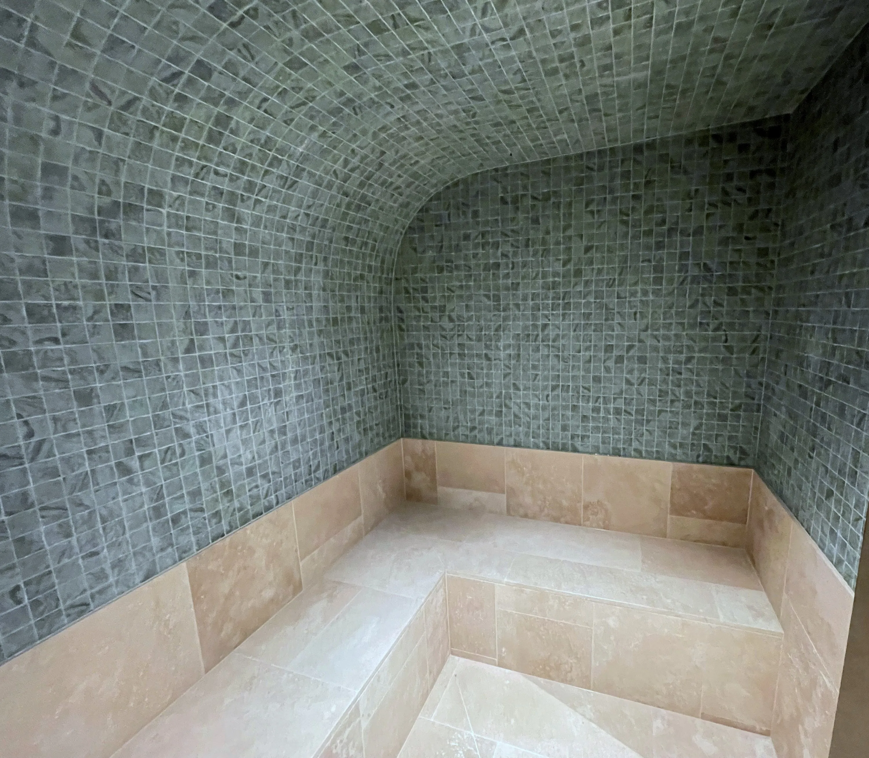 Mosaic vault curving down to a pale stone bench in a home steam room