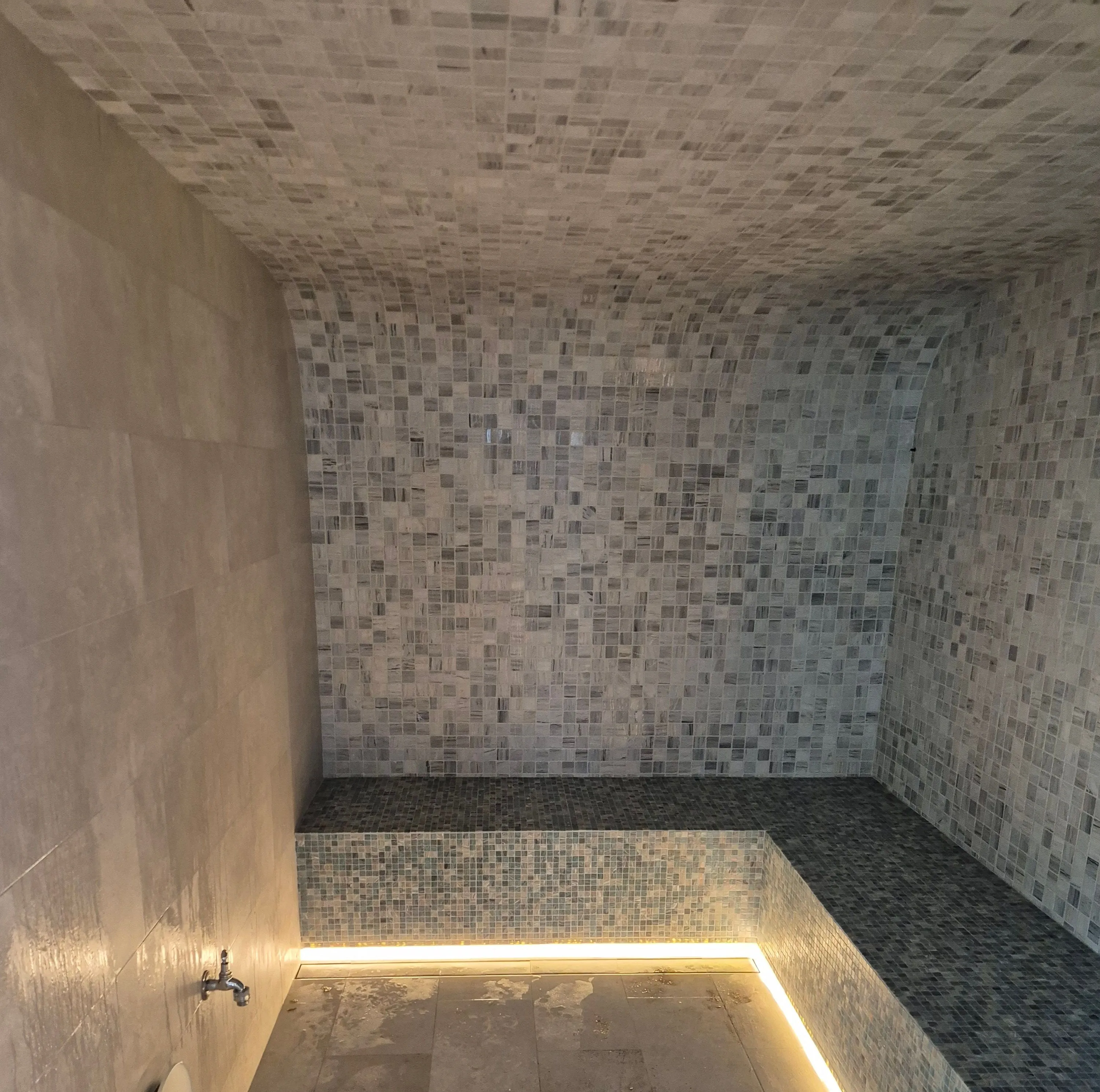 Vaulted mosaic steam room with an L-shaped bench lit along its base