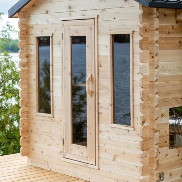 Close view of cabin sauna front: glass-panel door with wooden handle between two narrow vertical windows, interlocking log corners