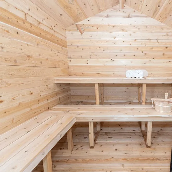 Cabin sauna interior with horizontal knotty light timber walls, peaked ceiling, two-tier benches, rolled towels and a wooden bucket