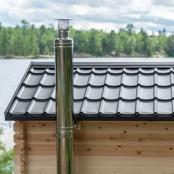 Stainless steel chimney flue rising past a black metal tile roof, lake and forest behind
