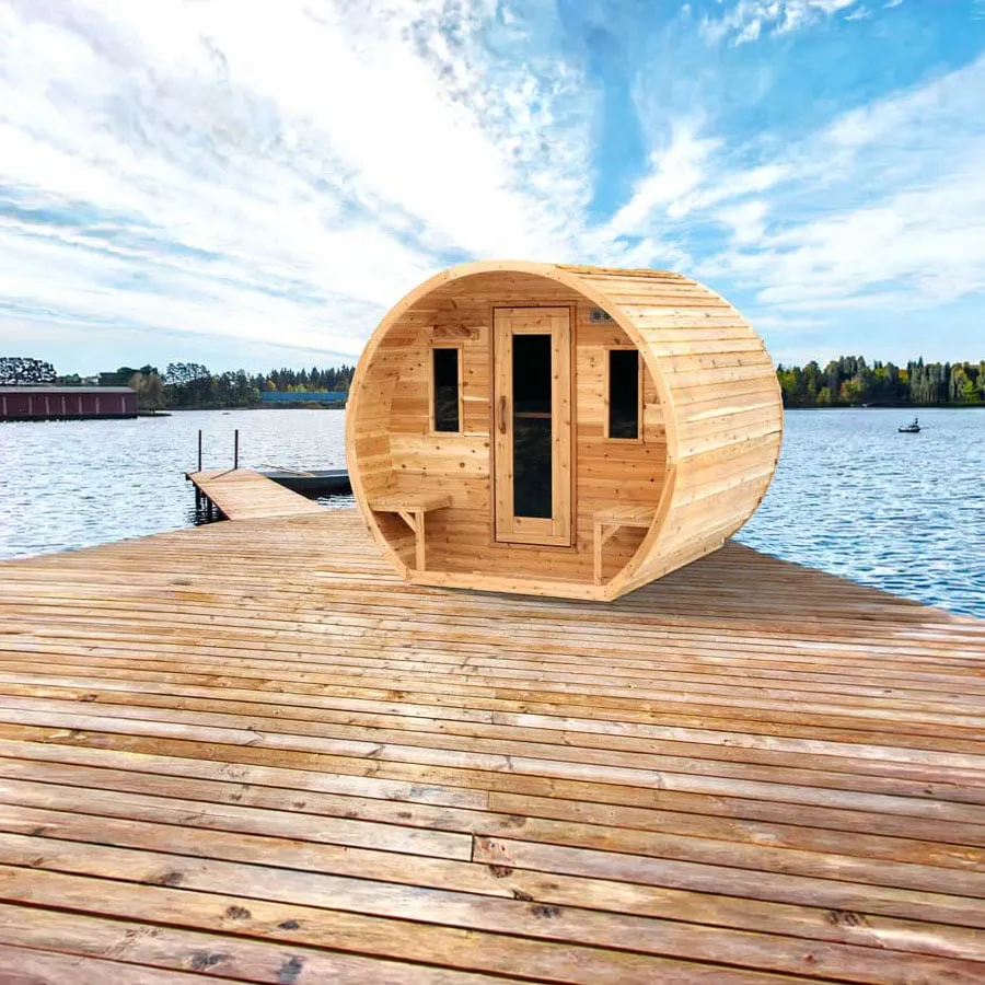 Barrel sauna in light knotty cedar with recessed front porch, fold-down porch benches, glass-panel door and two small windows, on a lakeside timber dock (composited scene).