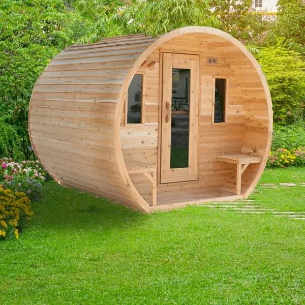 Three-quarter view of a light knotty cedar barrel sauna with front porch, two porch benches, glass-panel door and two windows, on a garden lawn with flower beds.